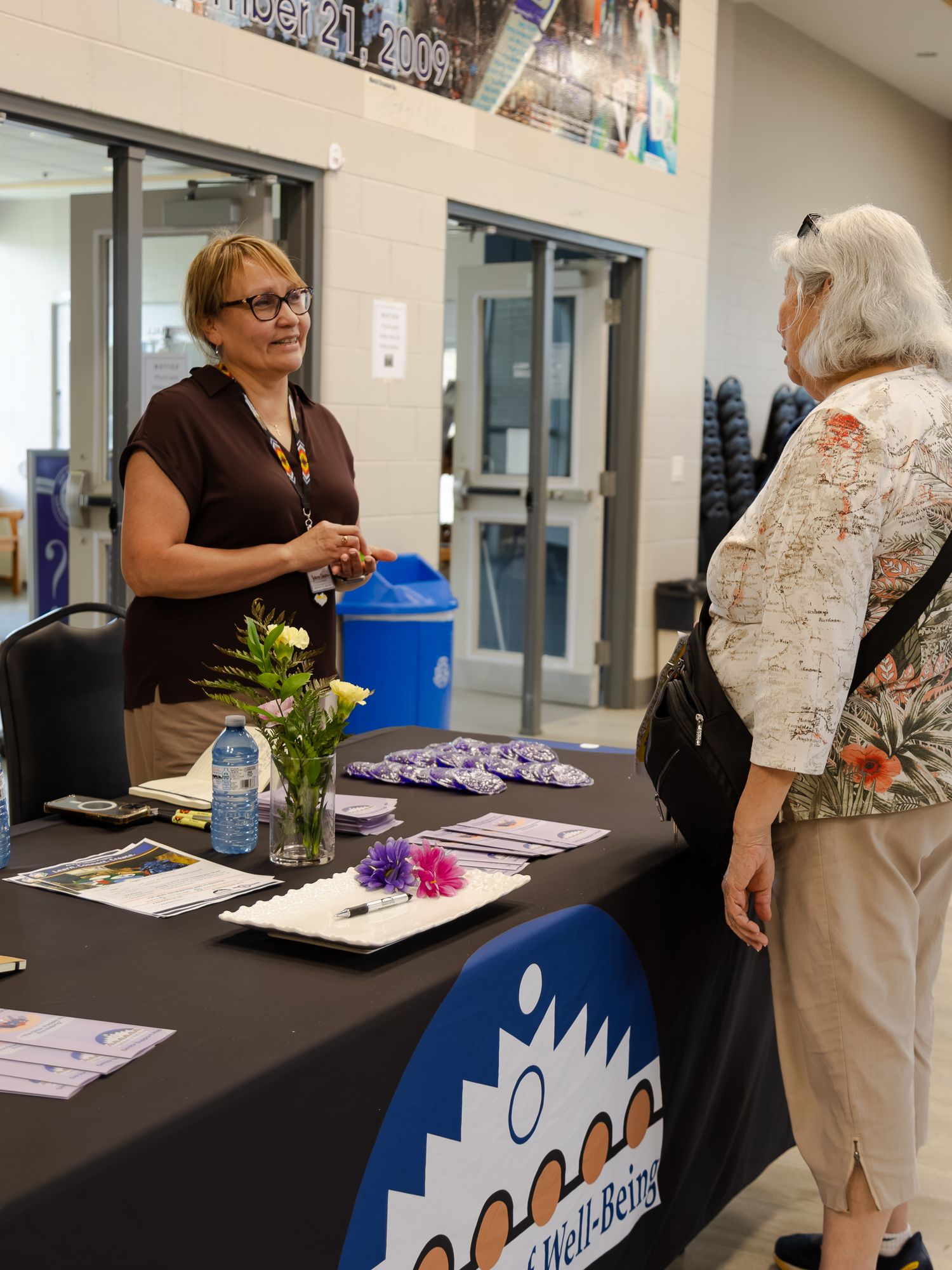 Healthcare worker at a Well-Being information table speaking with a visitor at a community event.