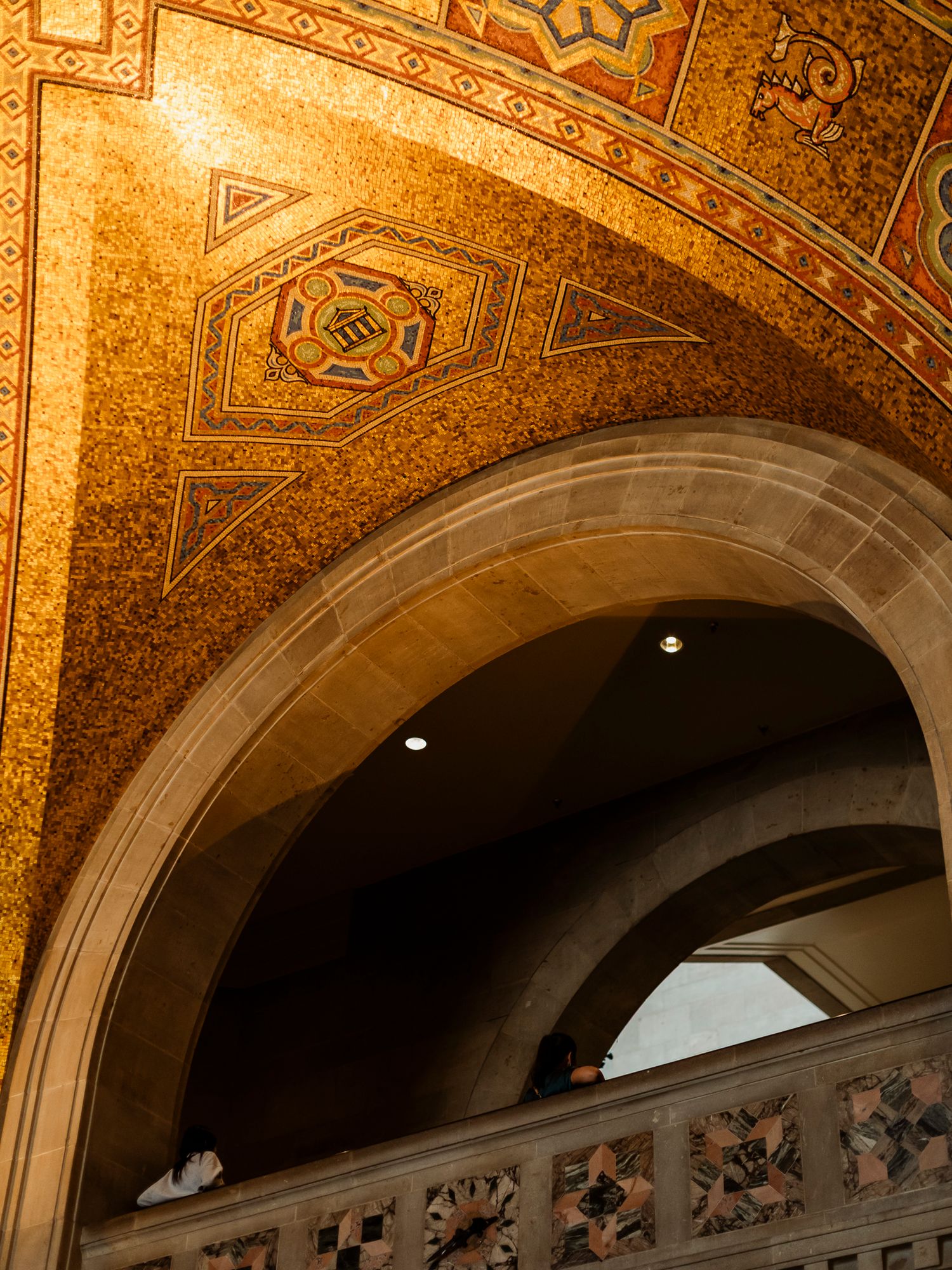 Ornate golden mosaic ceiling with geometric patterns above a stone arch in a historic building.