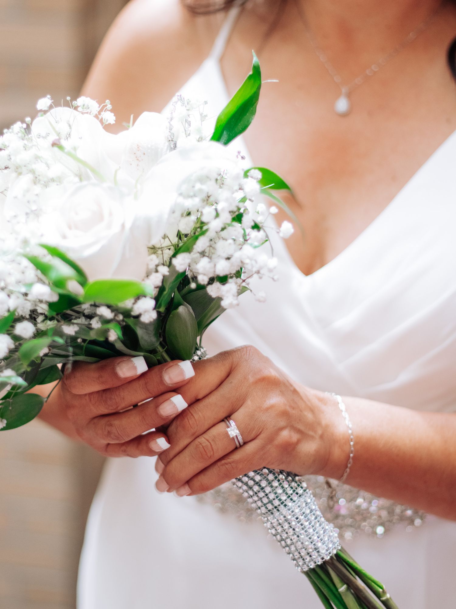 Bridal bouquet of white flowers with crystal wrap held by hands wearing wedding rings.