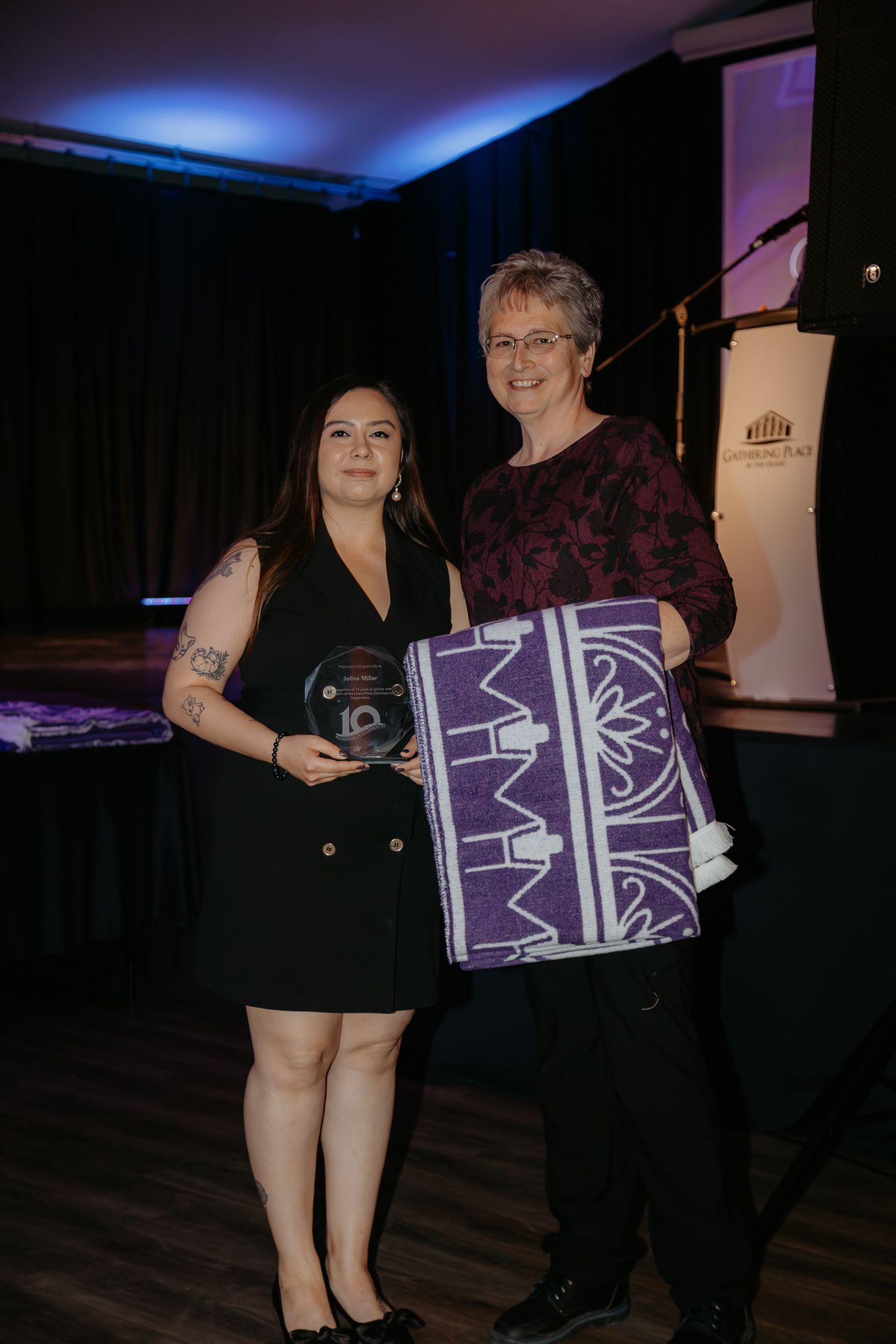 People holding purple and white patterned gift boxes at an indoor event.
