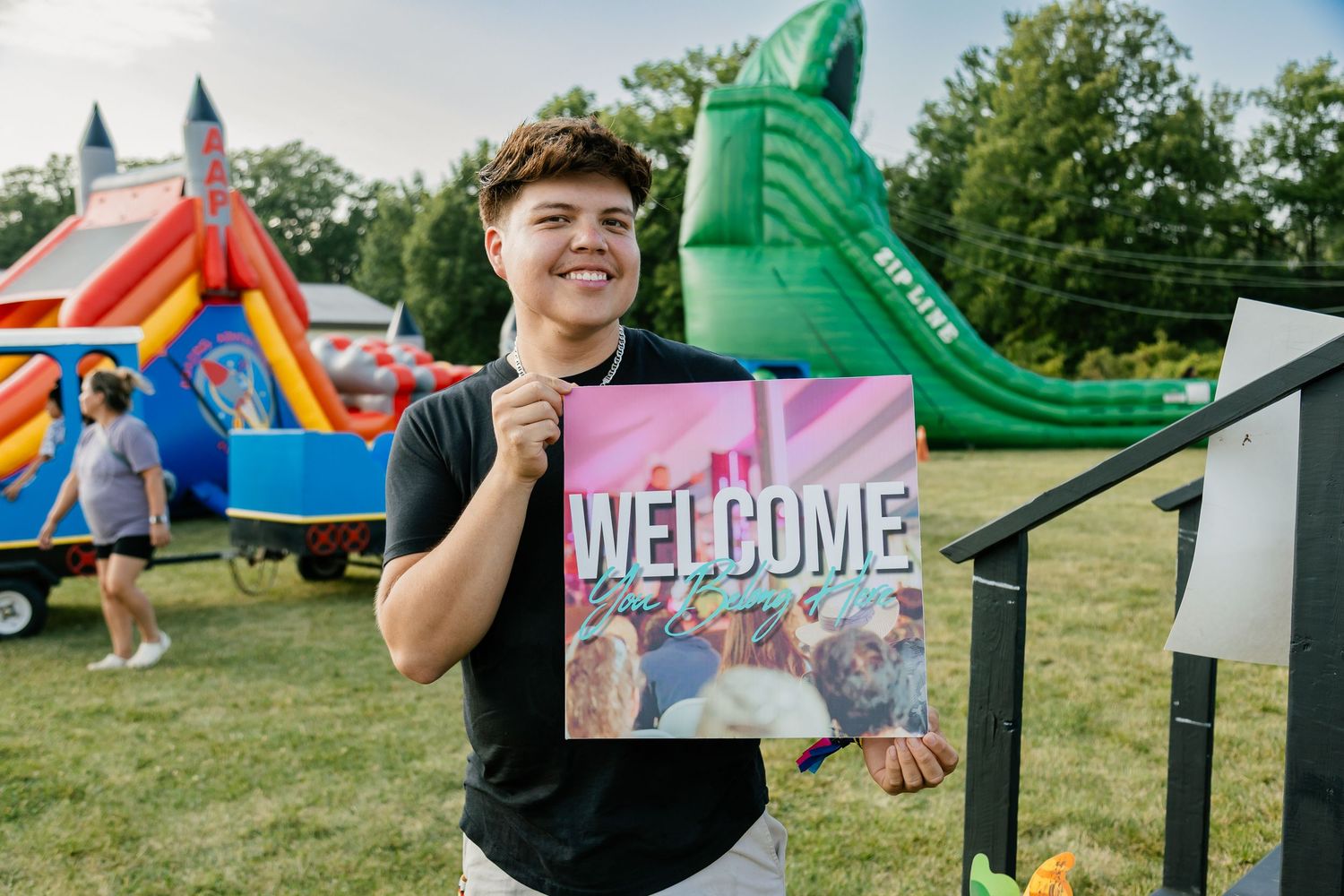A welcome sign holder stands in front of colorful bounce houses and inflatable slides at an outdoor event.