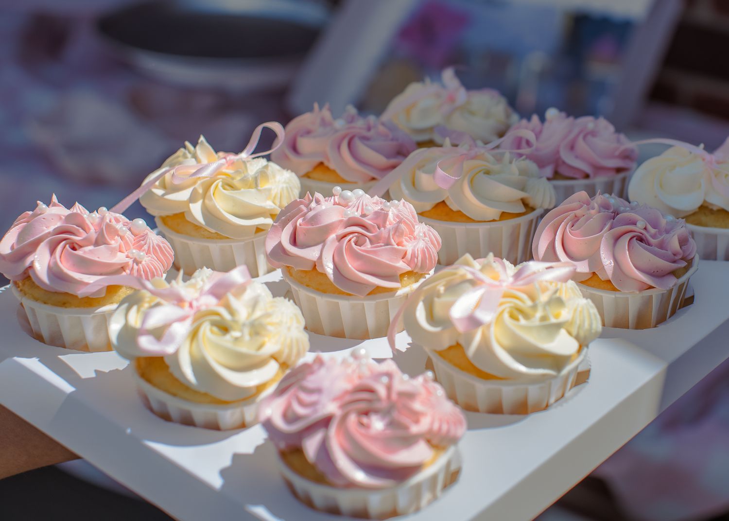 Elegant pink and white swirled frosting cupcakes arranged on a white tray for a celebration.