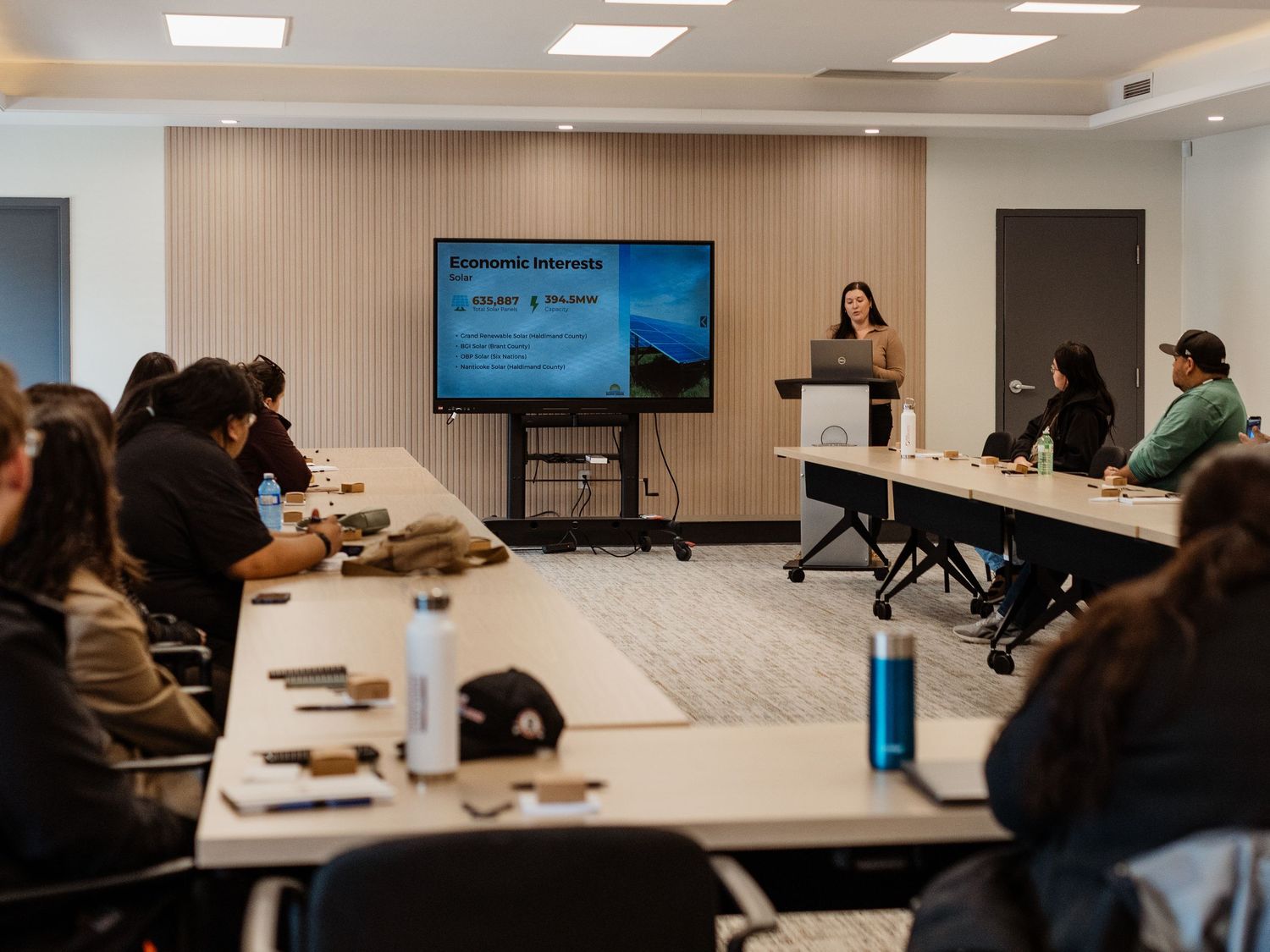 Professional presentation on Economic Interests in a modern conference room with engaged audience and large display screen.