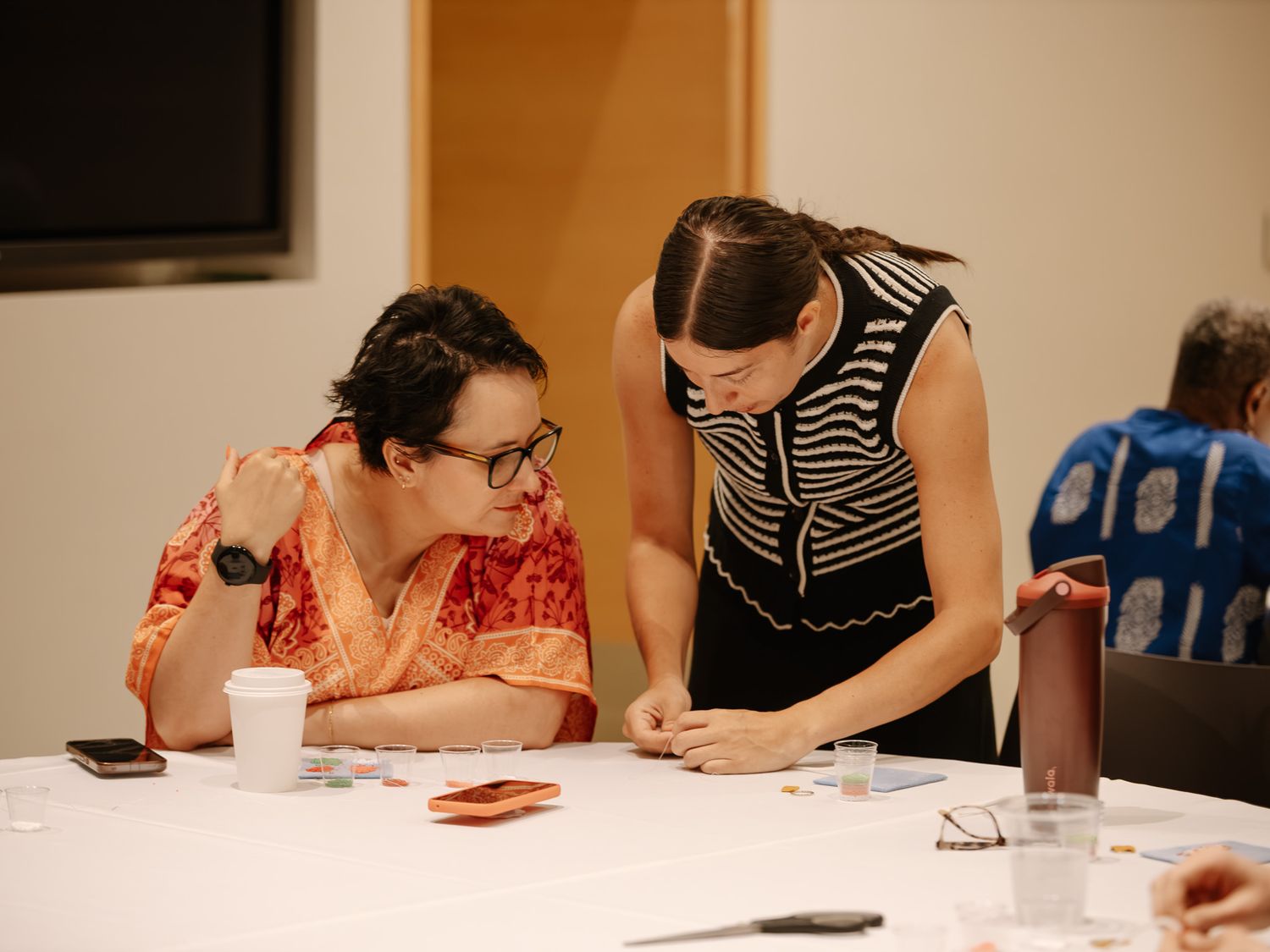 Two women collaborating at conference table during professional workshop or business meeting event.