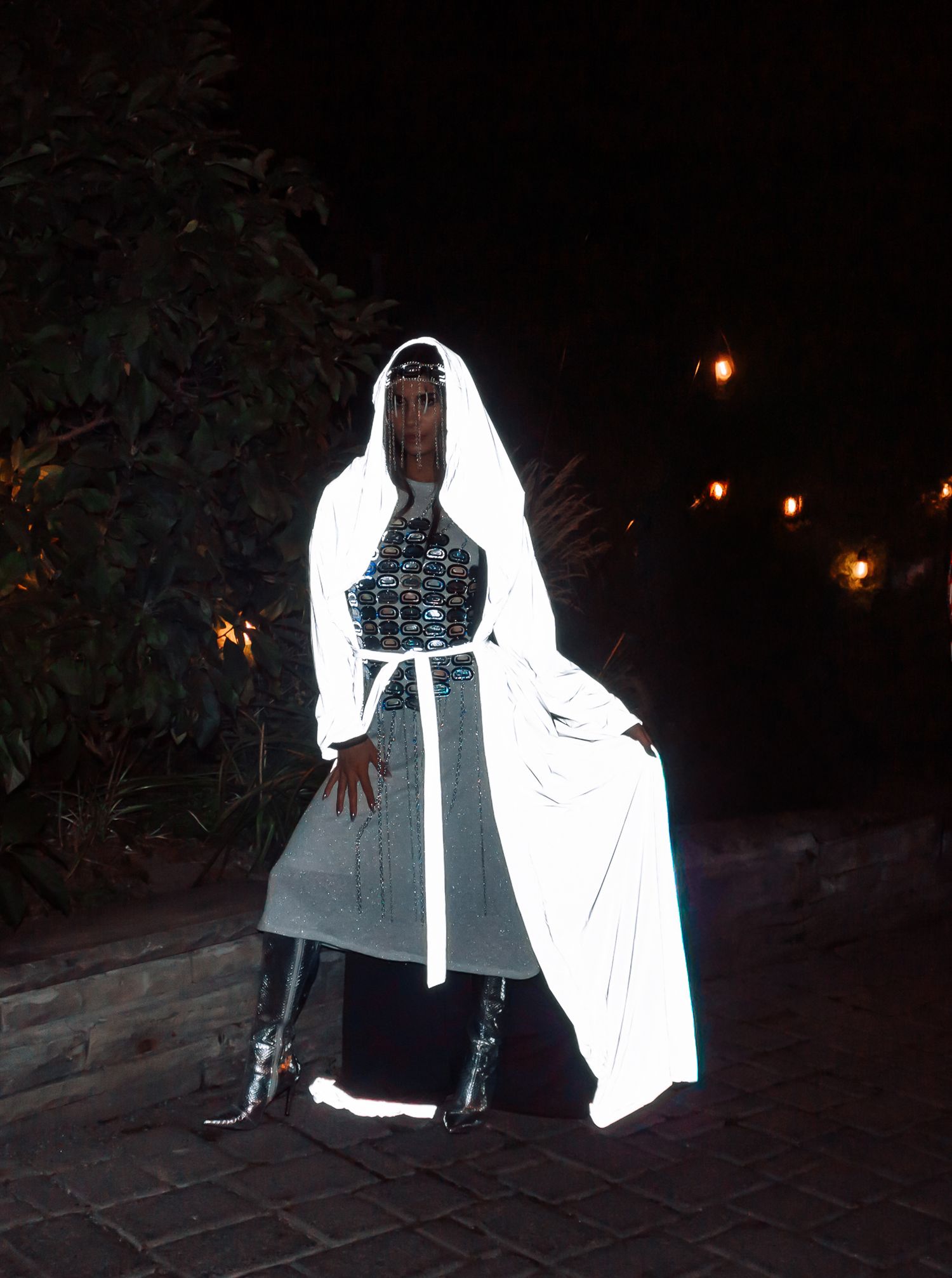 Model in reflective white hooded outfit and sequined top glows under night event lighting.