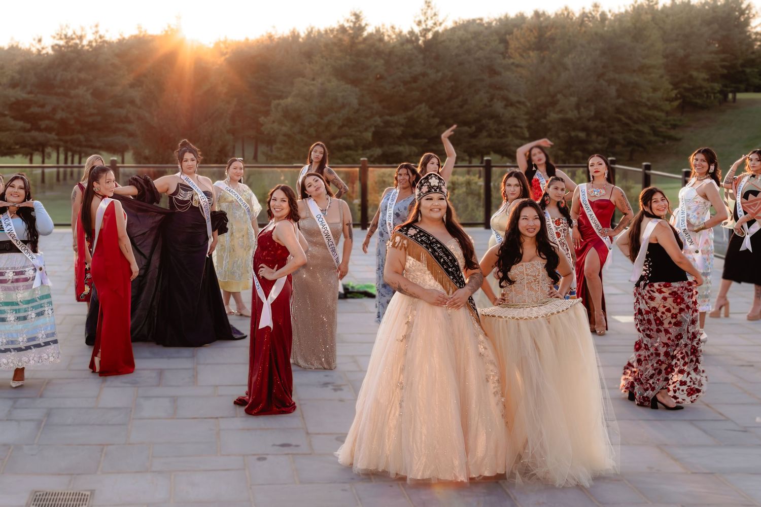 Group of pageant contestants in formal gowns gathered outdoors at sunset during a beauty competition.