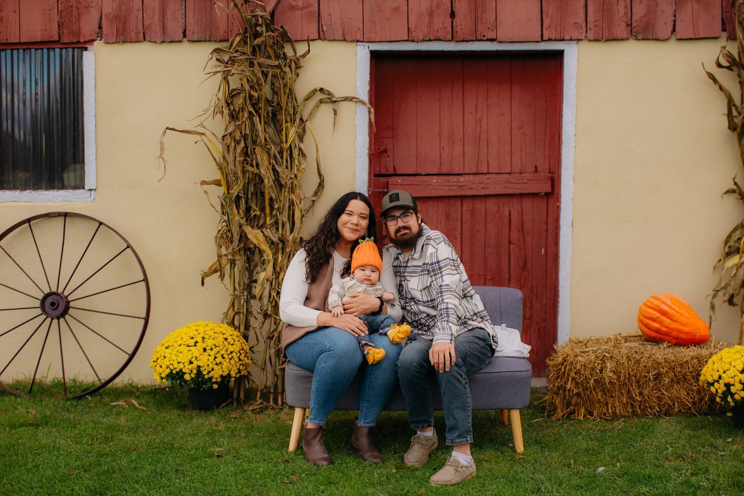 A family poses for photos in front of a rustic red barn with fall decorations and wagon wheels.