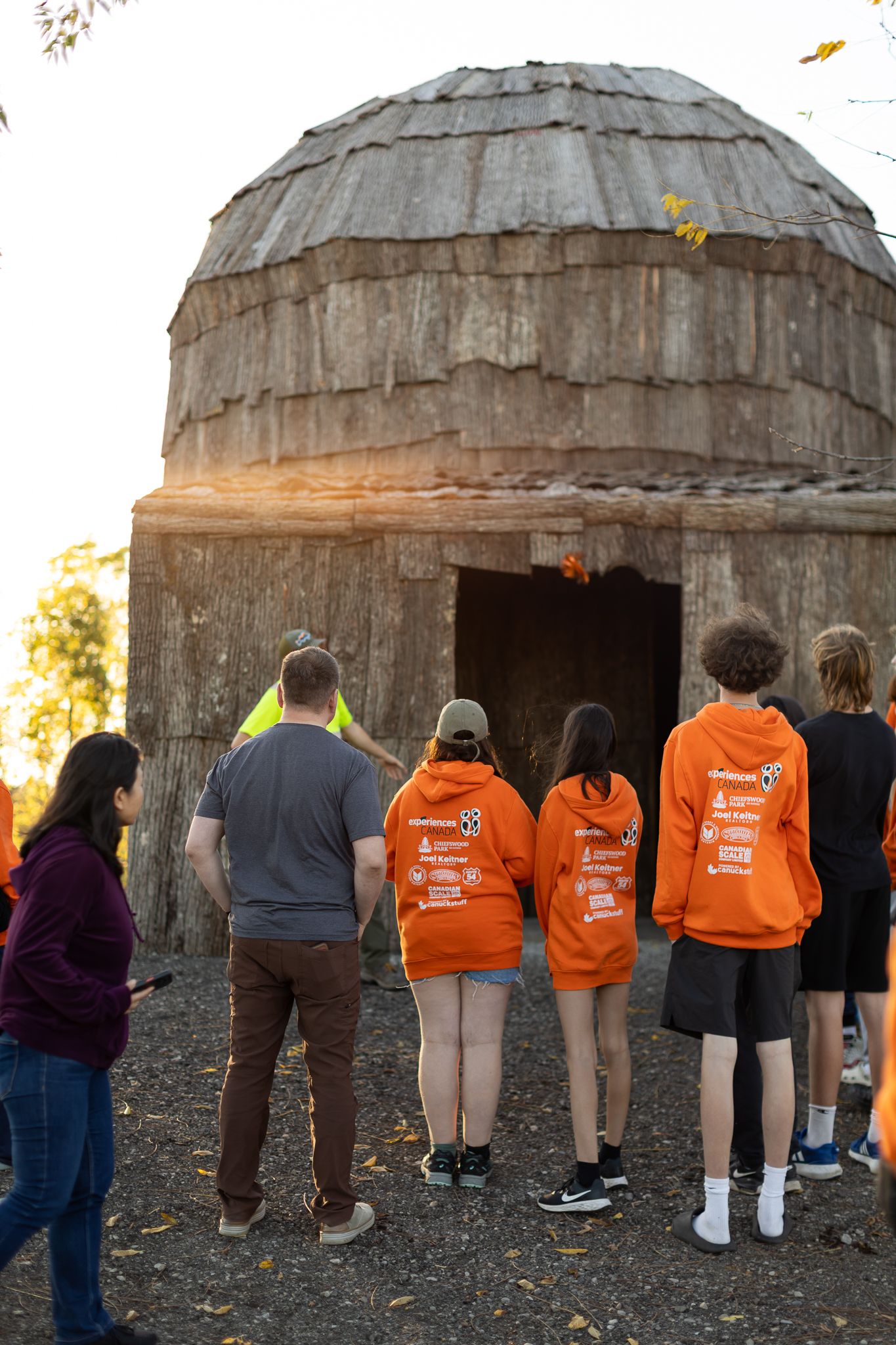 Group of people in orange shirts lined up looking through small openings in round dome-like structures at sunset.