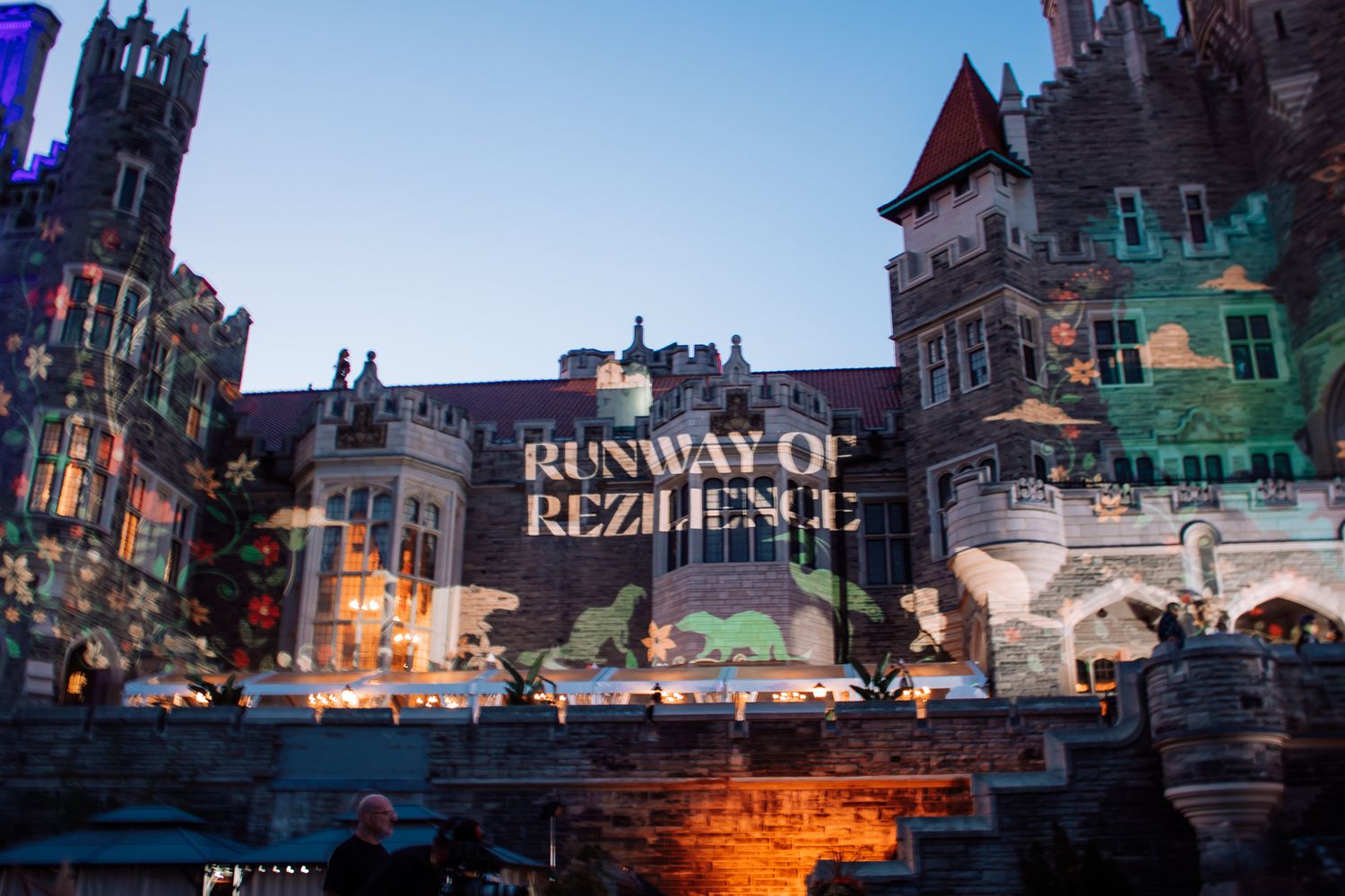 Casa Loma castle lit up at dusk with Runway of Rezilience projected on its facade.