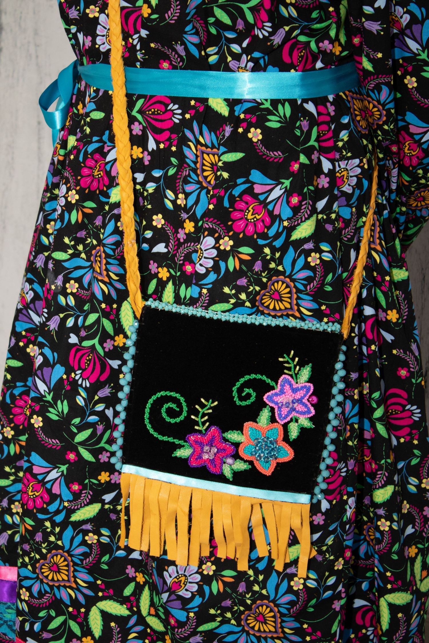 Black fabric bag with colorful floral pattern and yellow fringe trim against floral print background.