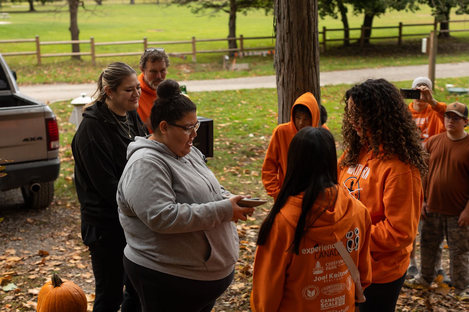 Group wearing bright orange sweatshirts gathered outdoors during an autumn day.