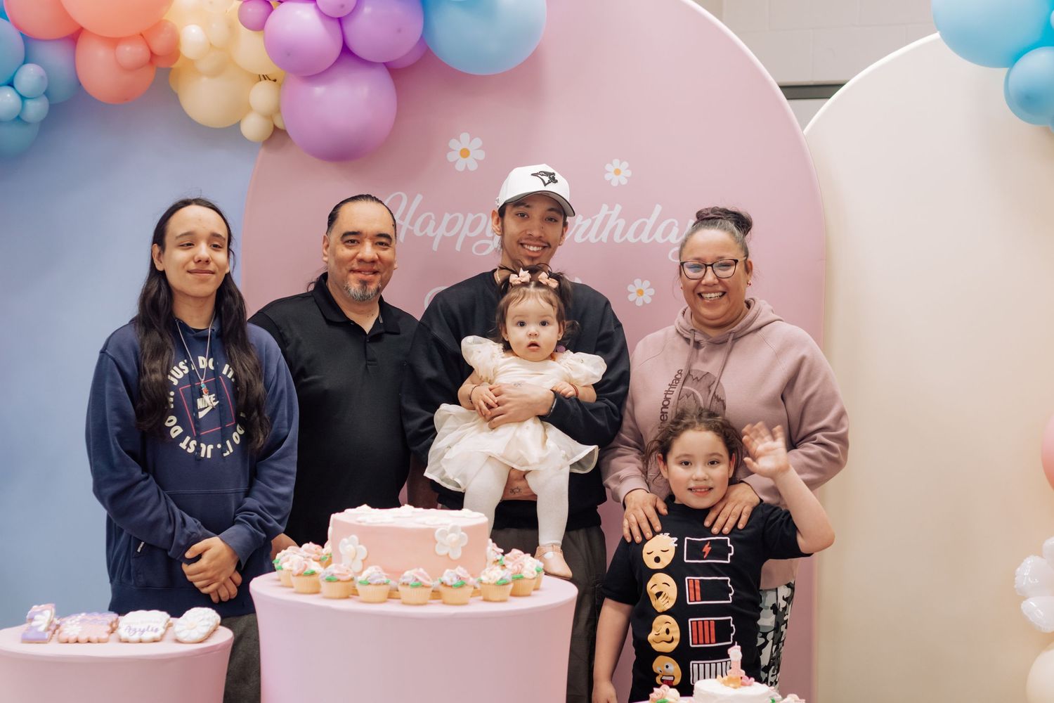 Birthday party gathering with pastel balloon arch and pink backdrop for celebrating a special day.