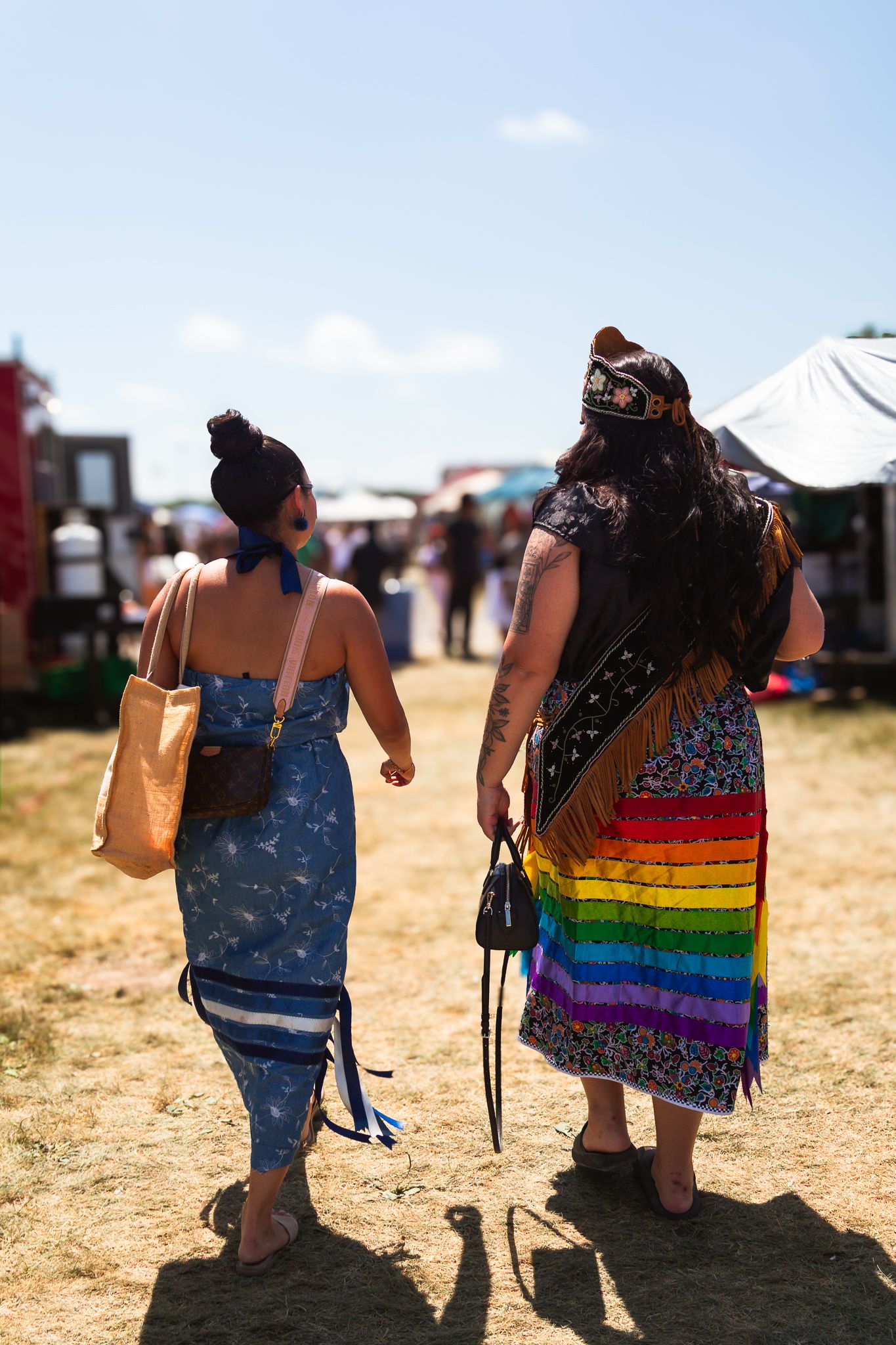 Festival attendees walking across sunny field carrying bags and supplies.