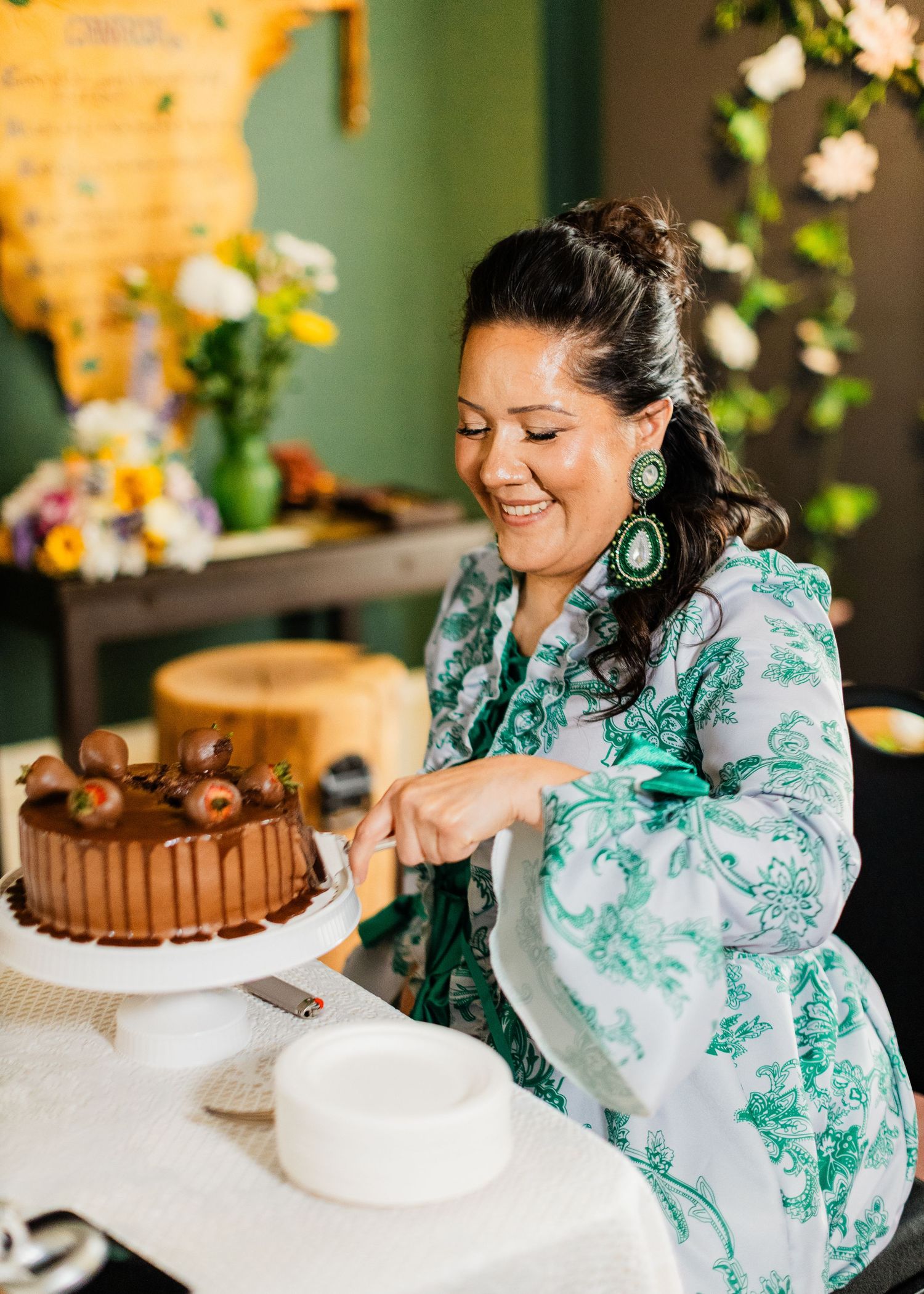Smiling woman in green floral dress cutting chocolate cake at elegant party celebration.