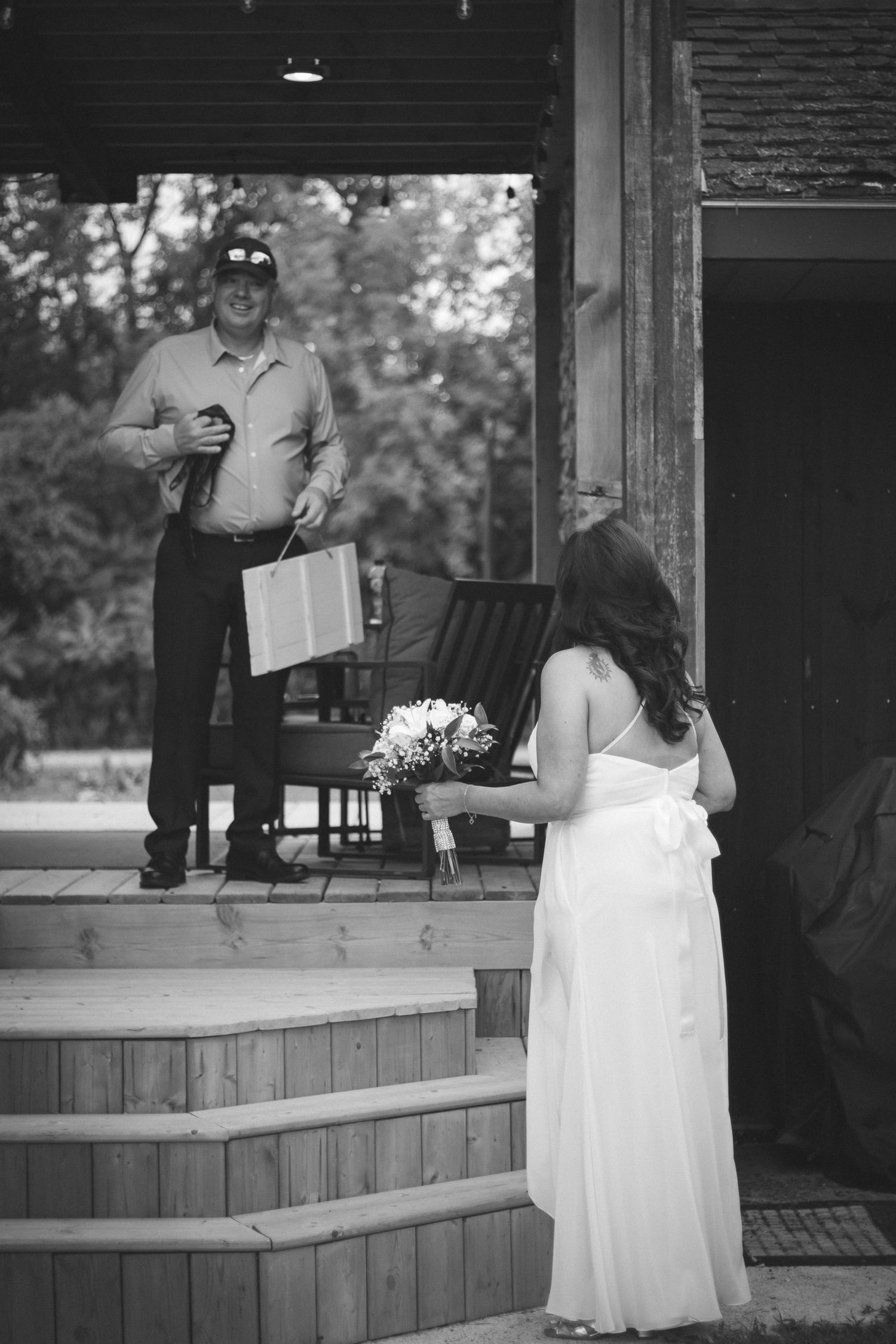 Bride in white gown meets groom on wooden porch steps in black and white wedding photo.