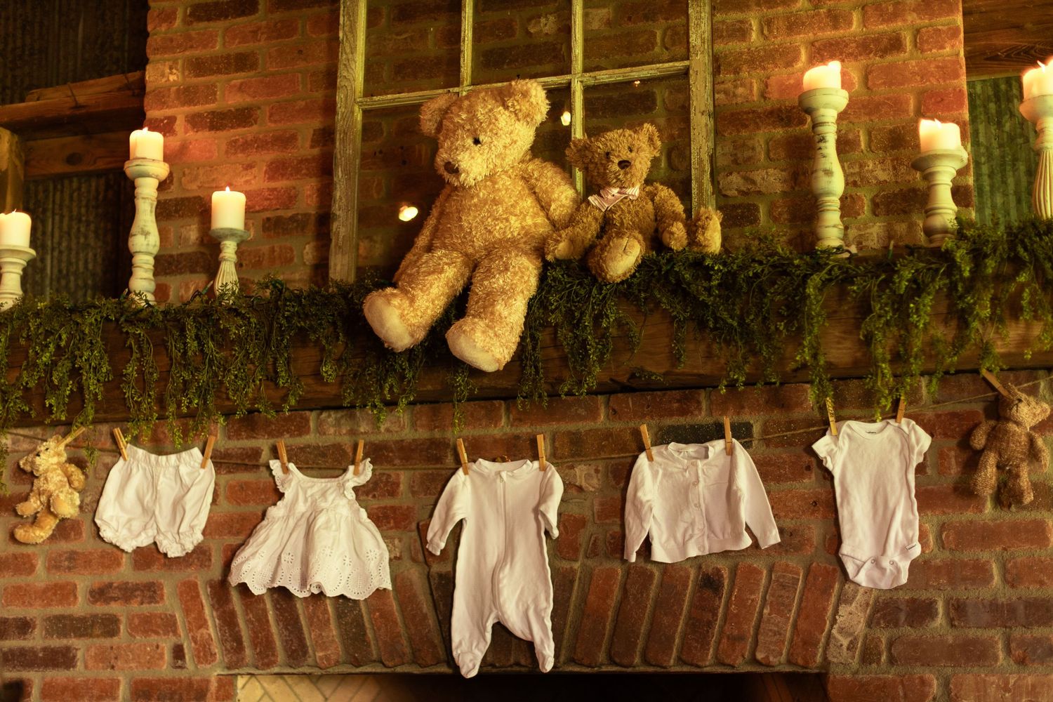 Baby clothes and teddy bears displayed on string lights for a rustic baby shower decoration.