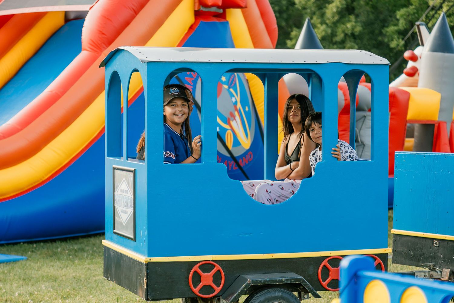 Children enjoying a ride in a bright blue train car at an outdoor carnival.