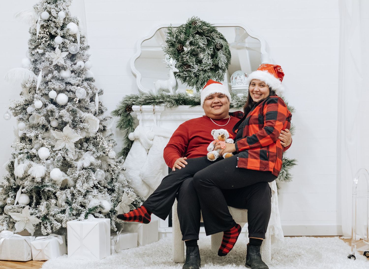 Holiday portrait session with matching red and black plaid outfits against white Christmas backdrop.