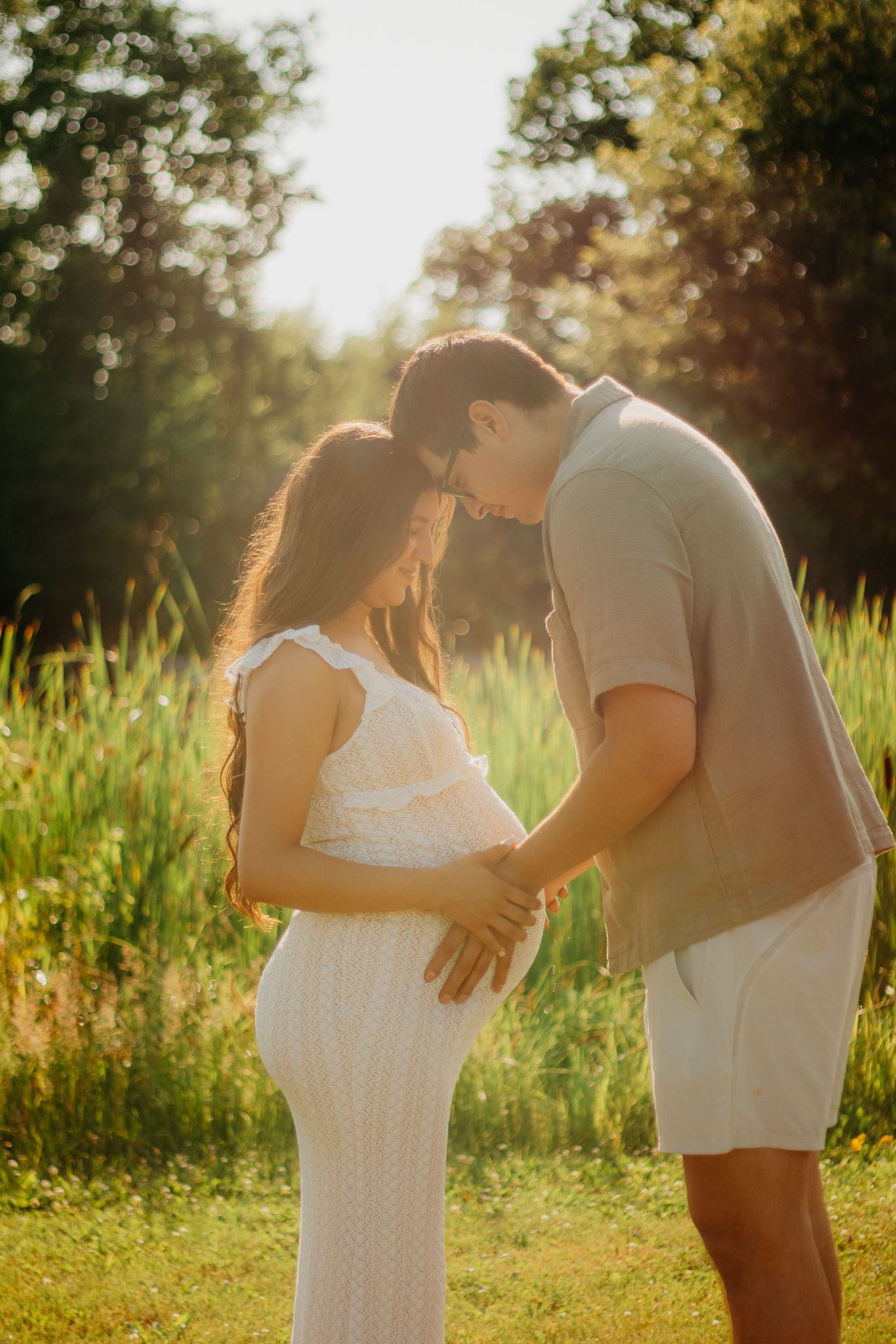Sun-drenched maternity portraits showing tender moments between a couple in a grassy field.