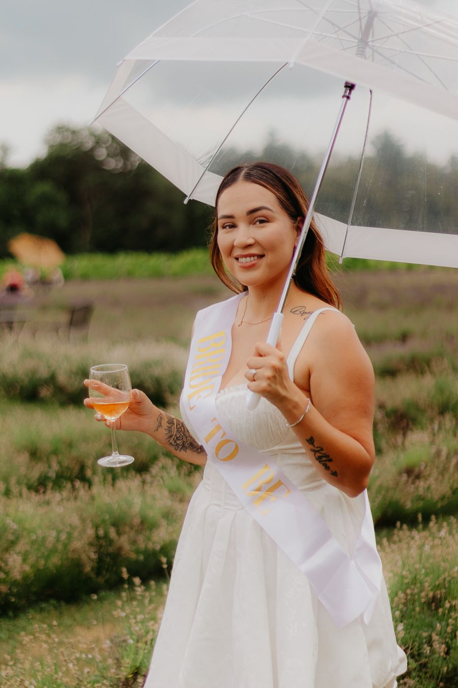 Woman in white dress holding clear umbrella and wine glass in outdoor garden setting.