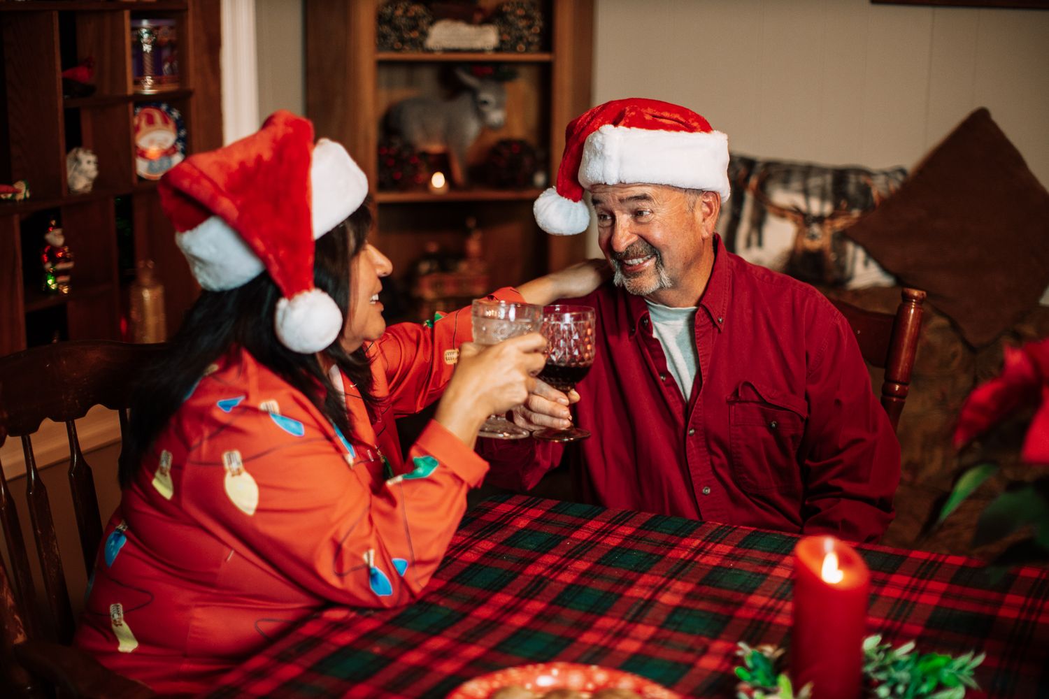 People wearing Santa hats gathered around a table with holiday decorations and plaid tablecloth.