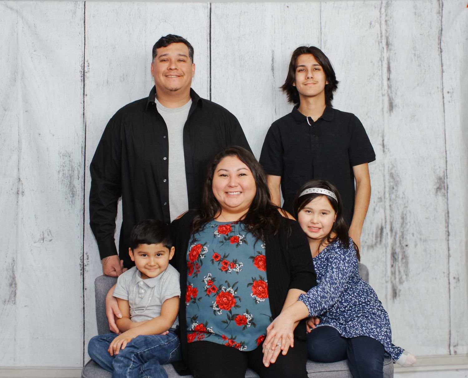 Family portrait session against a white wooden backdrop with casual coordinated outfits.