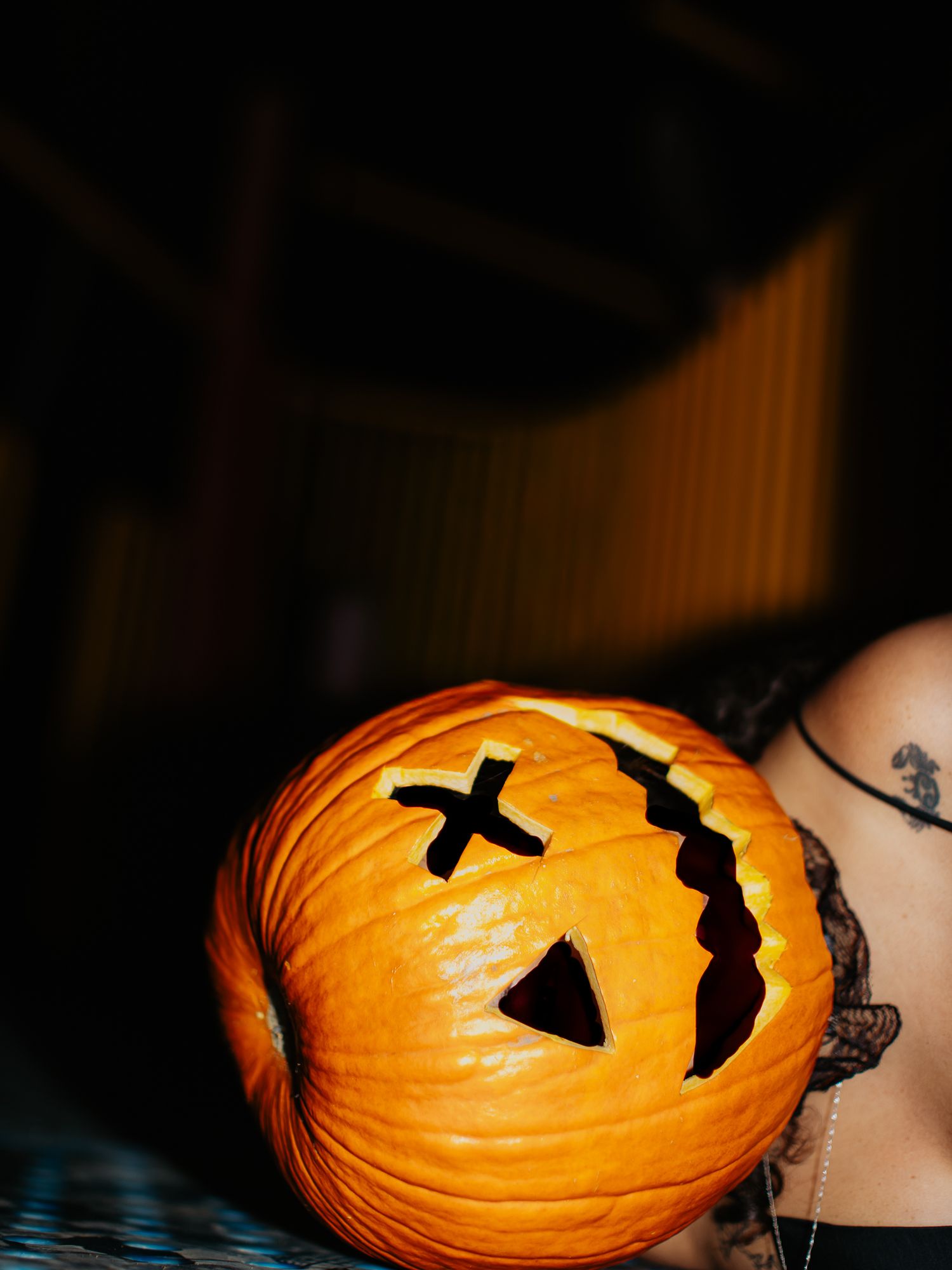 A carved Halloween pumpkin with an X-shaped eye glows orange in dark lighting.
