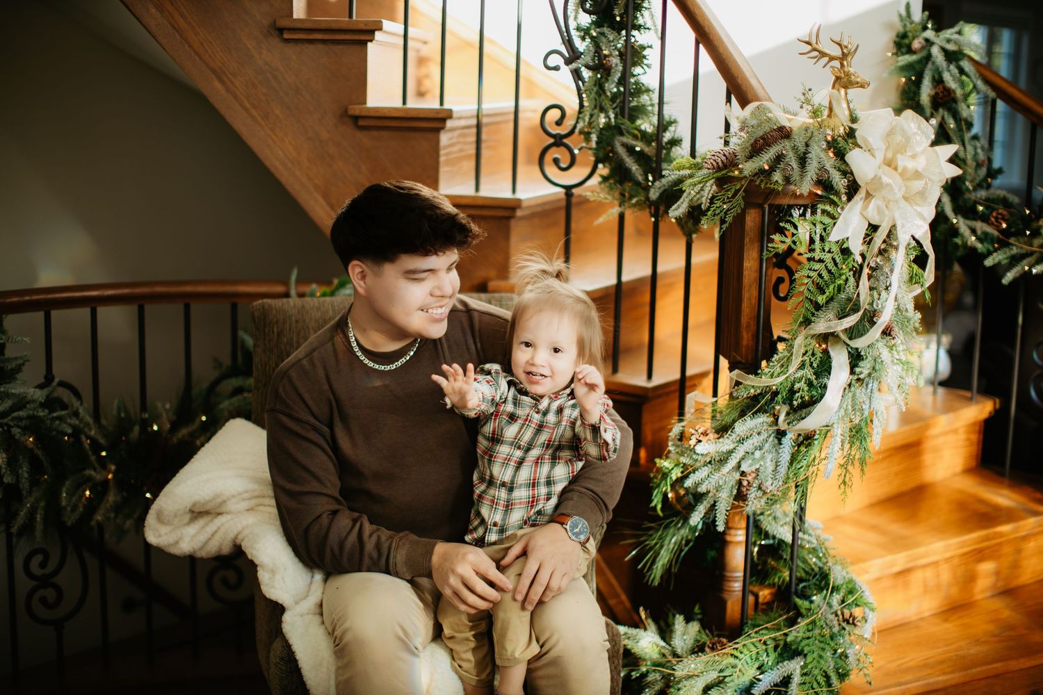 Cozy indoor portrait on wooden stairs decorated with holiday greenery.