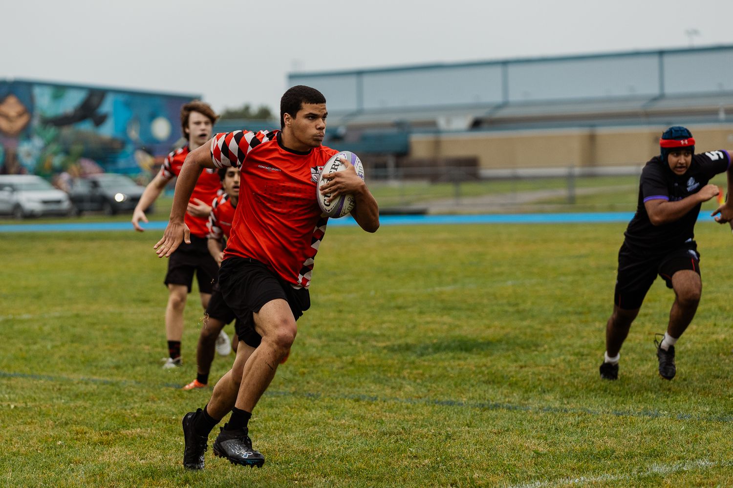 Rugby players in red and black jerseys compete on a grass field during an outdoor match.