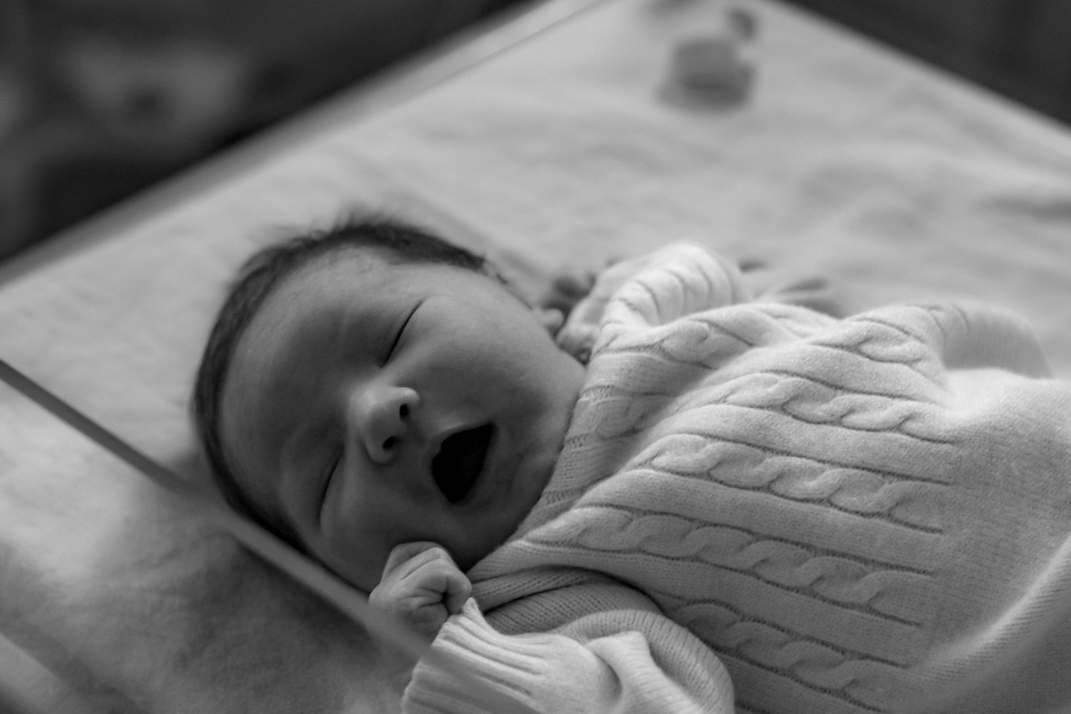 Peaceful newborn baby resting on white textured blanket in monochrome.