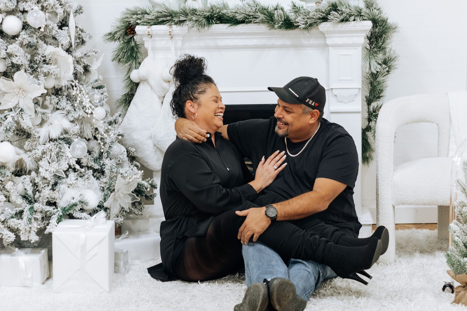 A couple shares an intimate moment in front of a decorated Christmas fireplace with flocked trees.