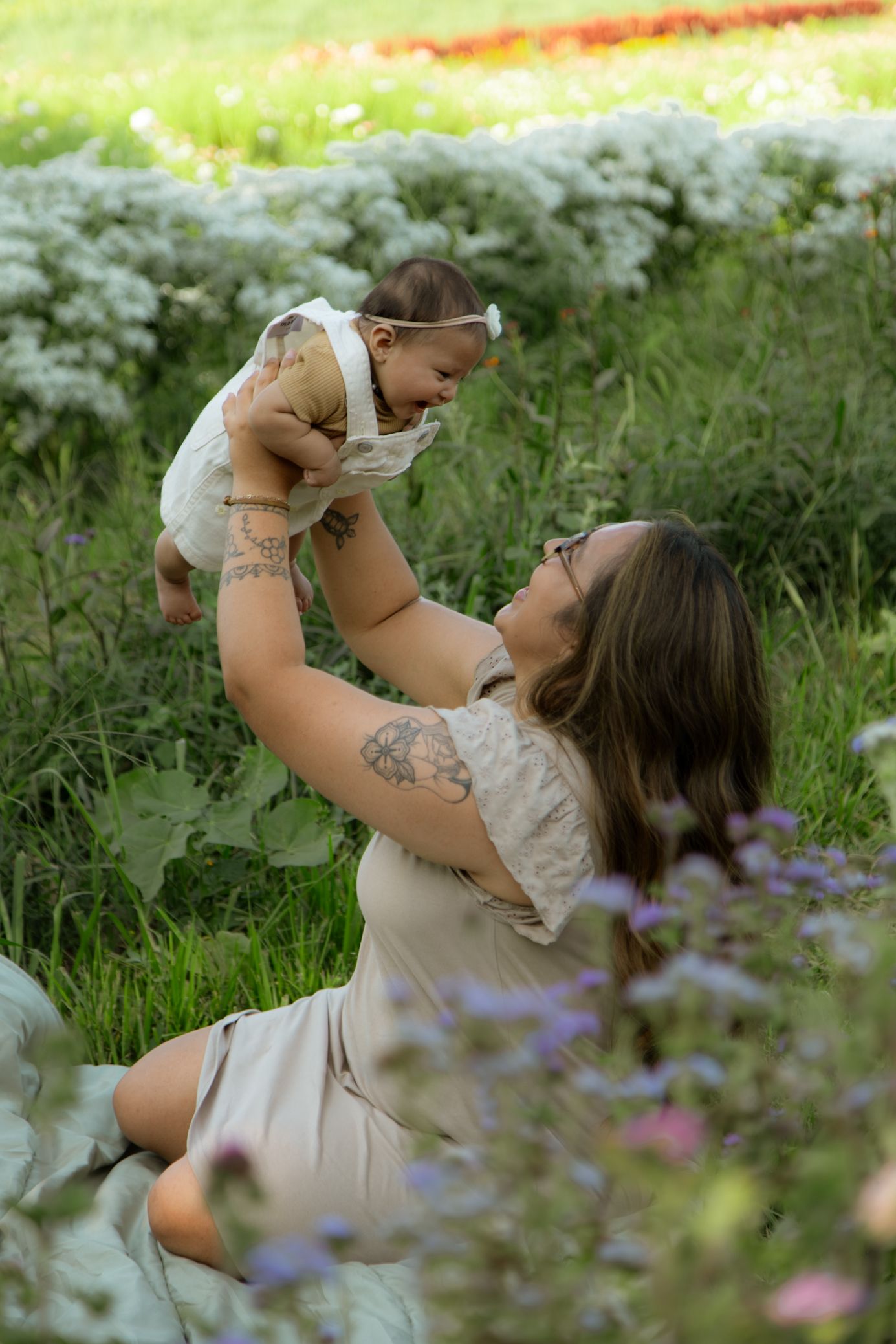 Playful moment between parent and baby surrounded by white flowers in a garden setting.