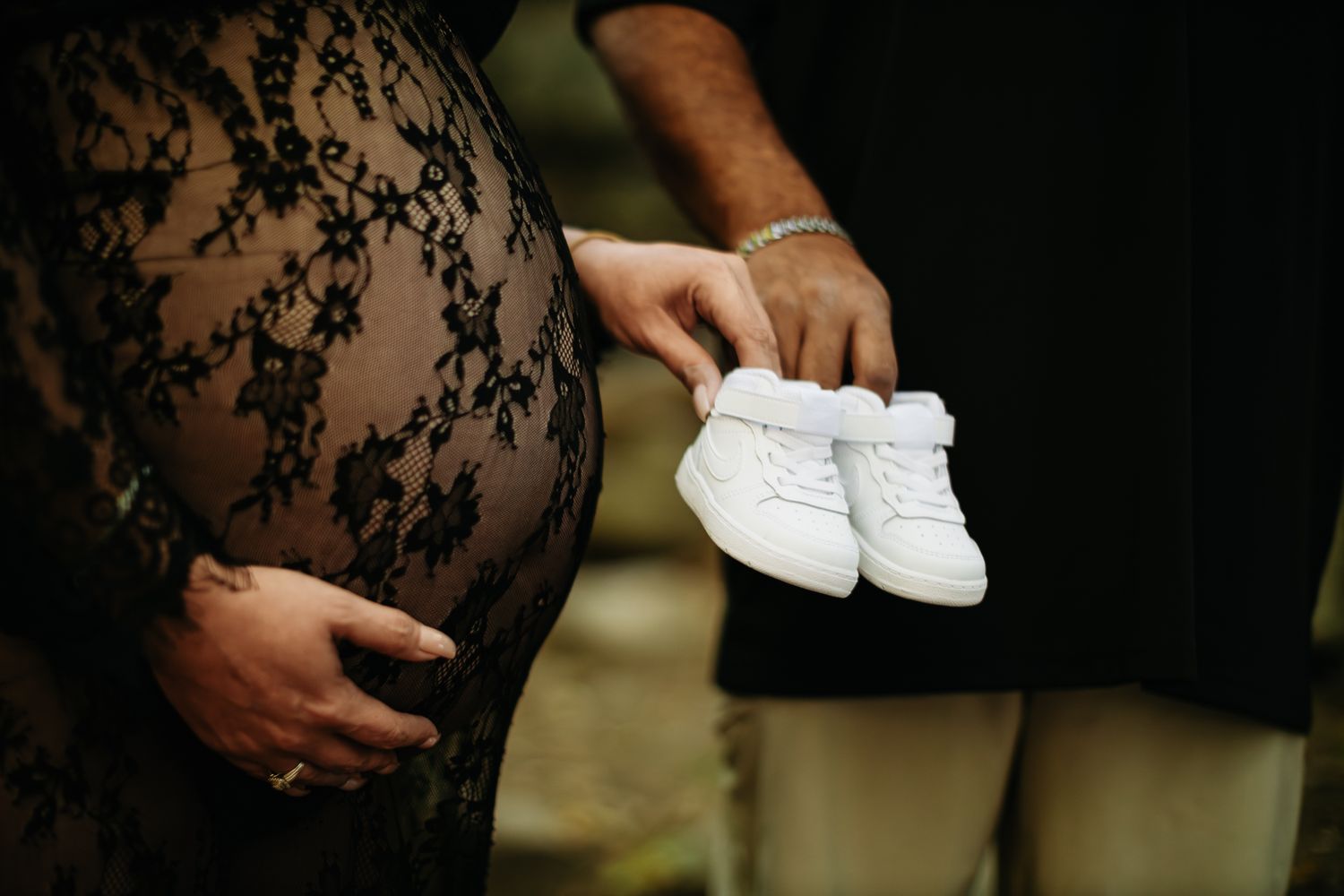 Close-up shot of couple holding tiny white baby shoes during their pregnancy announcement.