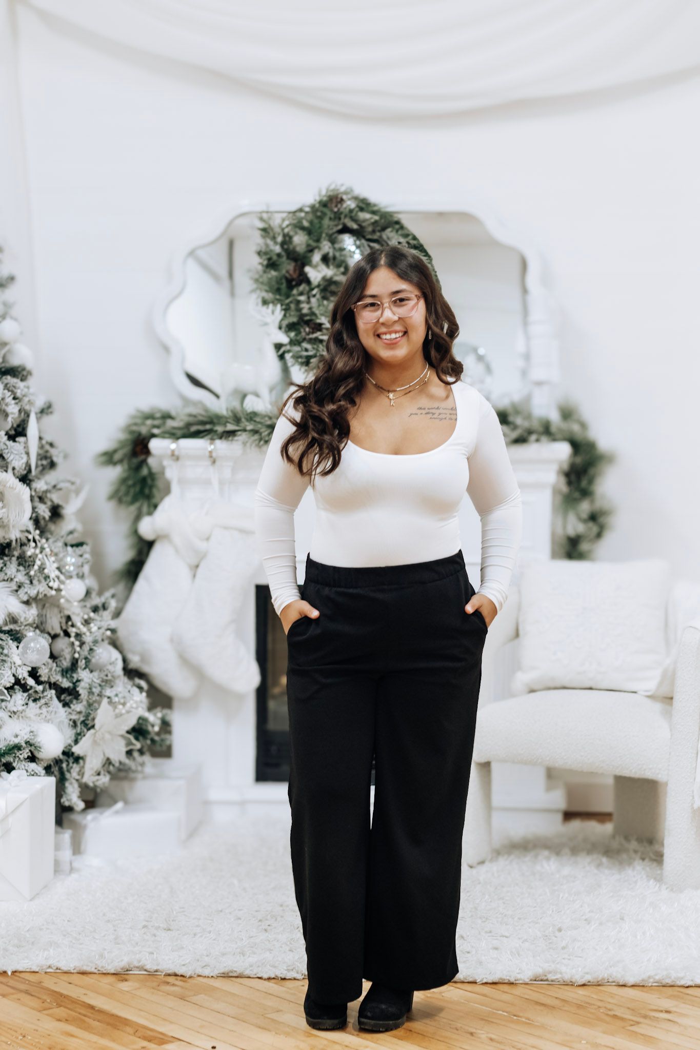 Fashion photoshoot featuring a white sweater and black pants outfit against a winter-themed backdrop.