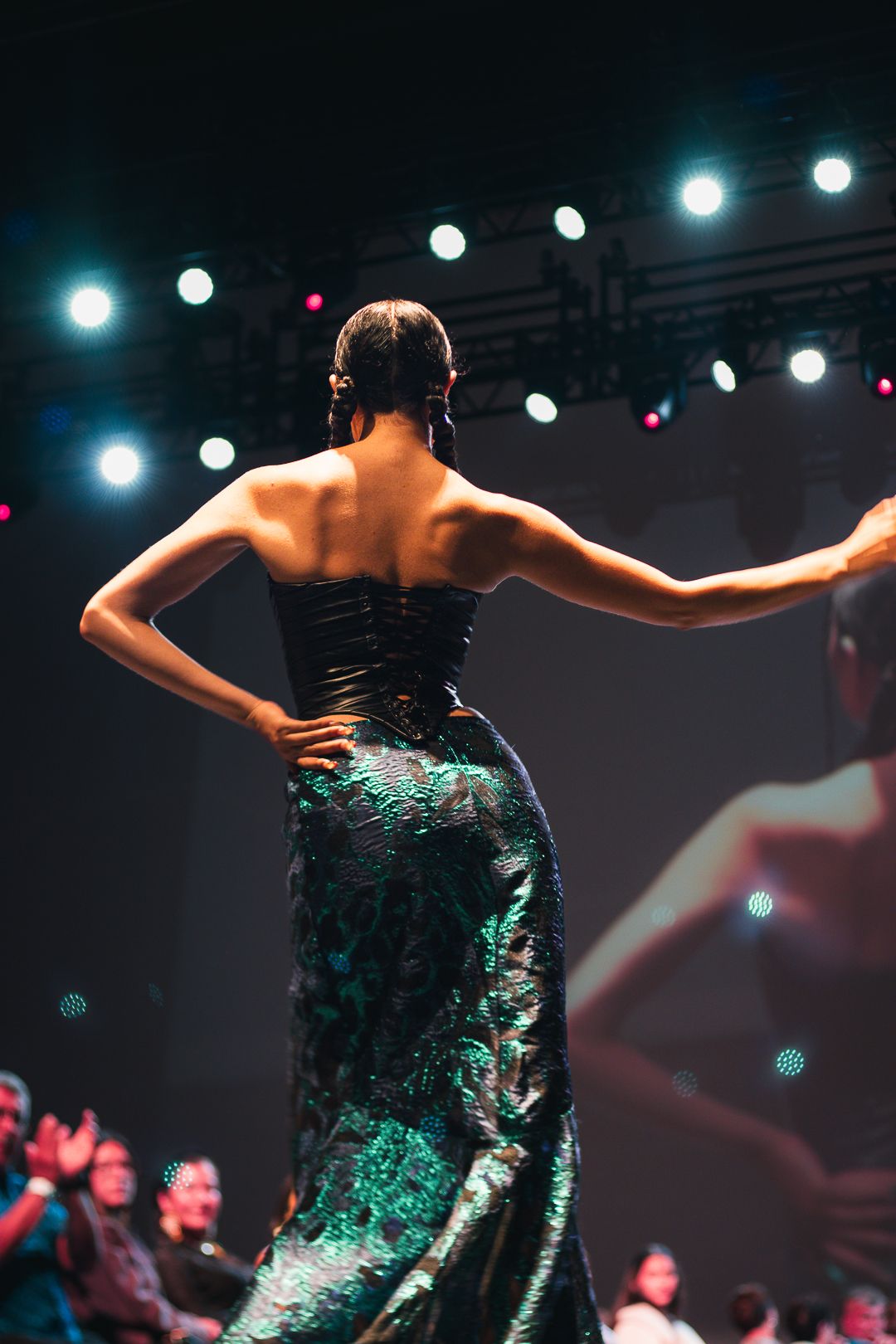 Performer in sparkly teal dress on stage with dramatic lighting and spotlights.