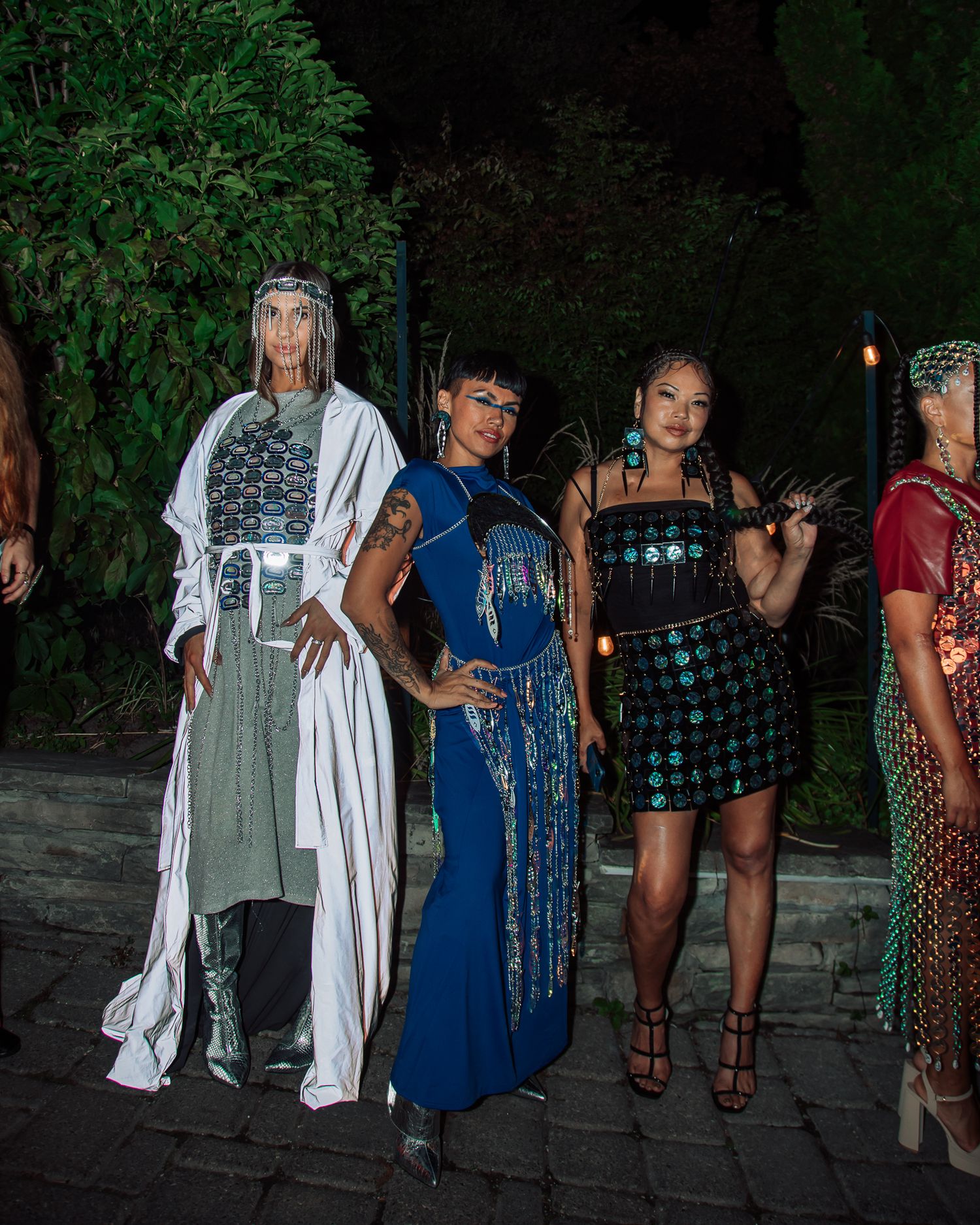 Group photo of models wearing diverse evening wear styles against a dark outdoor backdrop.