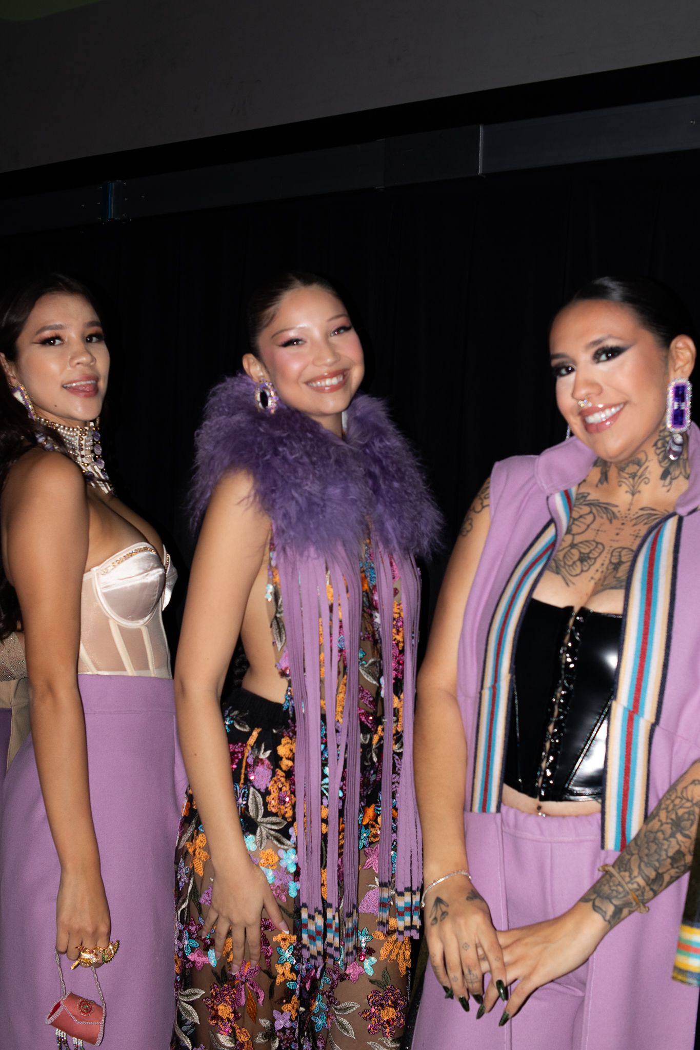 Group wearing coordinated purple dresses and feather boas posing together on stage.