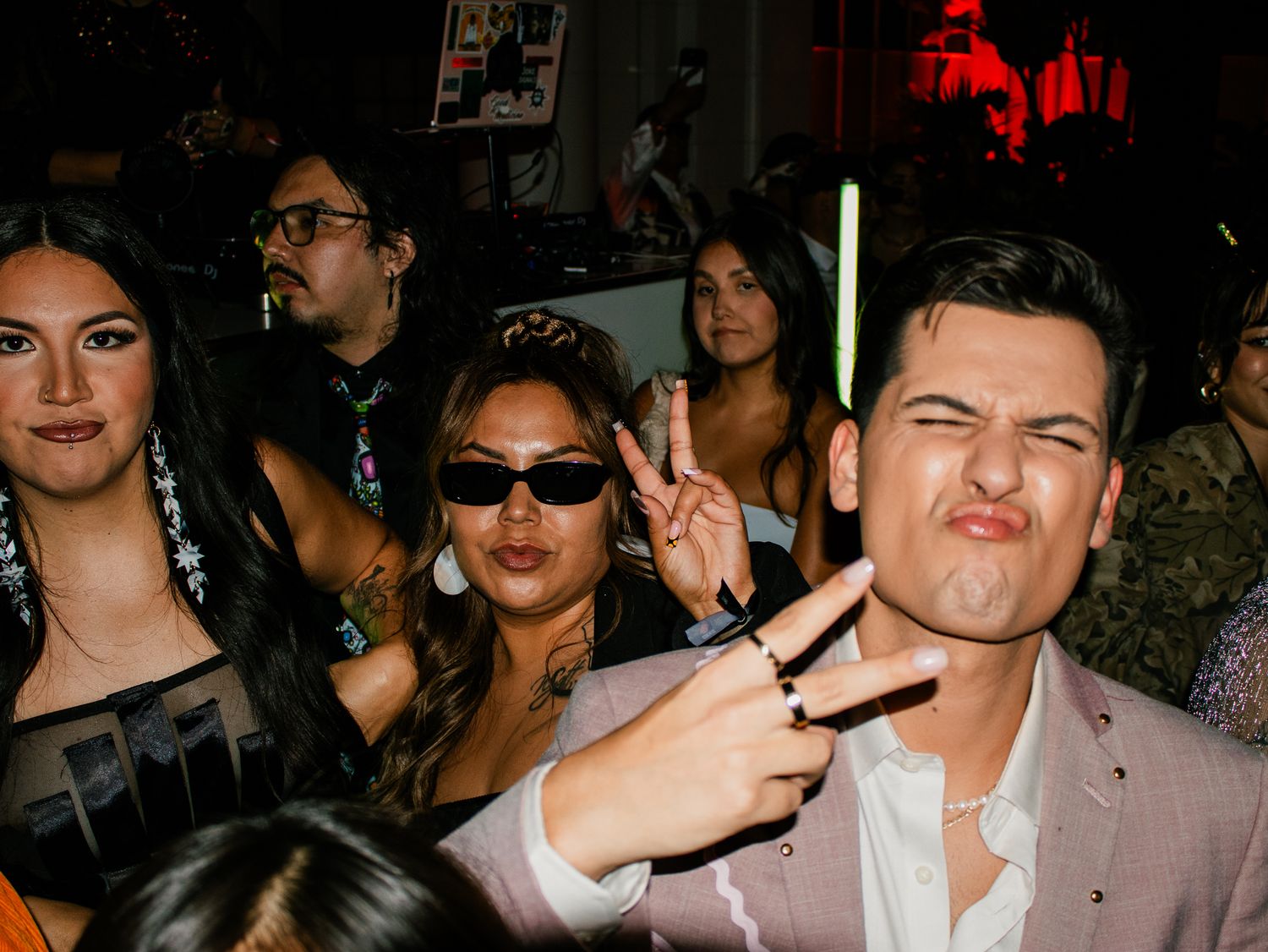 Group of friends posing at a lively party, making peace signs and fun faces in a dimly lit venue.
