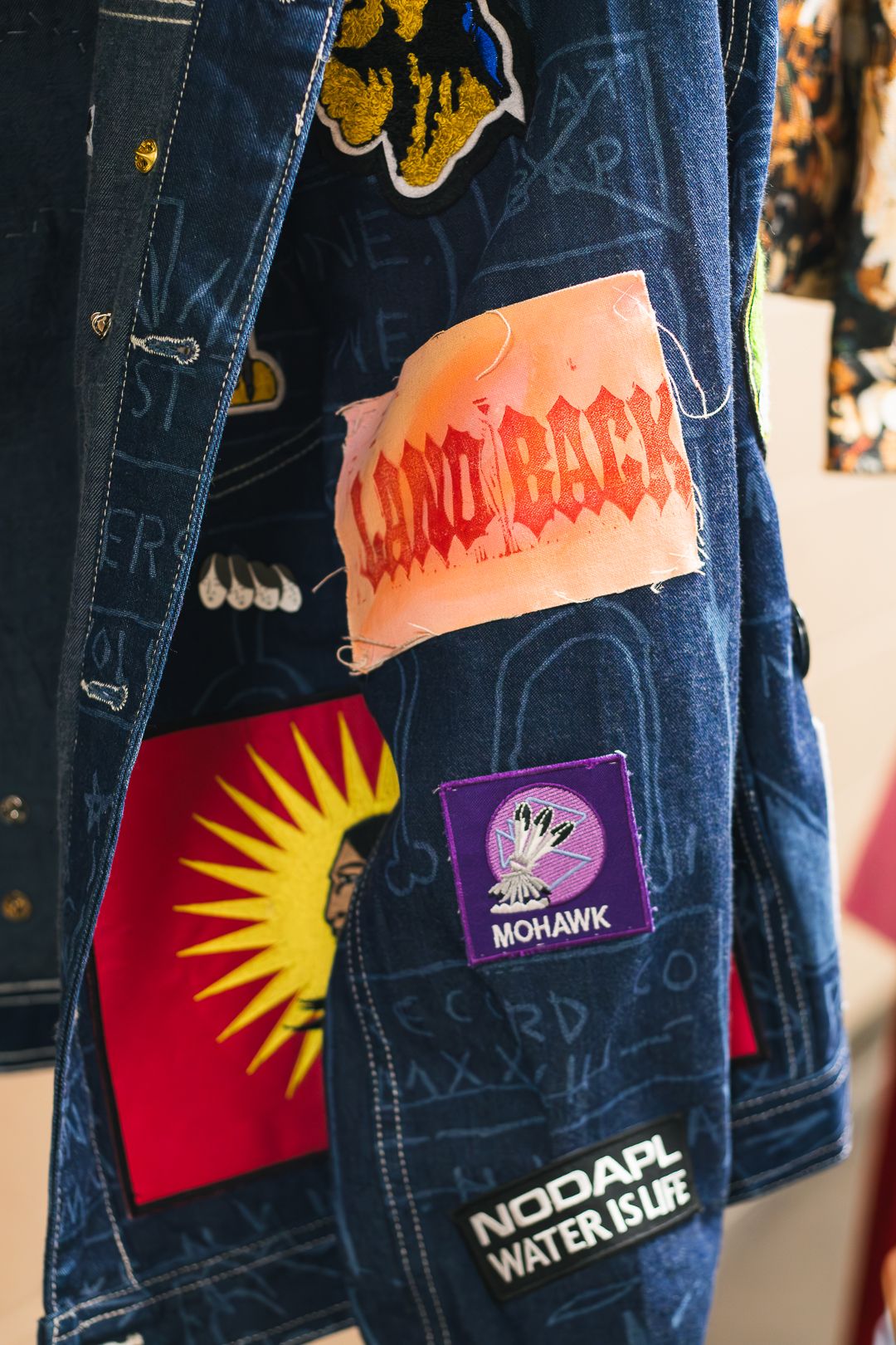 Denim jacket with Indigenous patches including Land Back, Mohawk, and NODAPL Water is Life slogans.