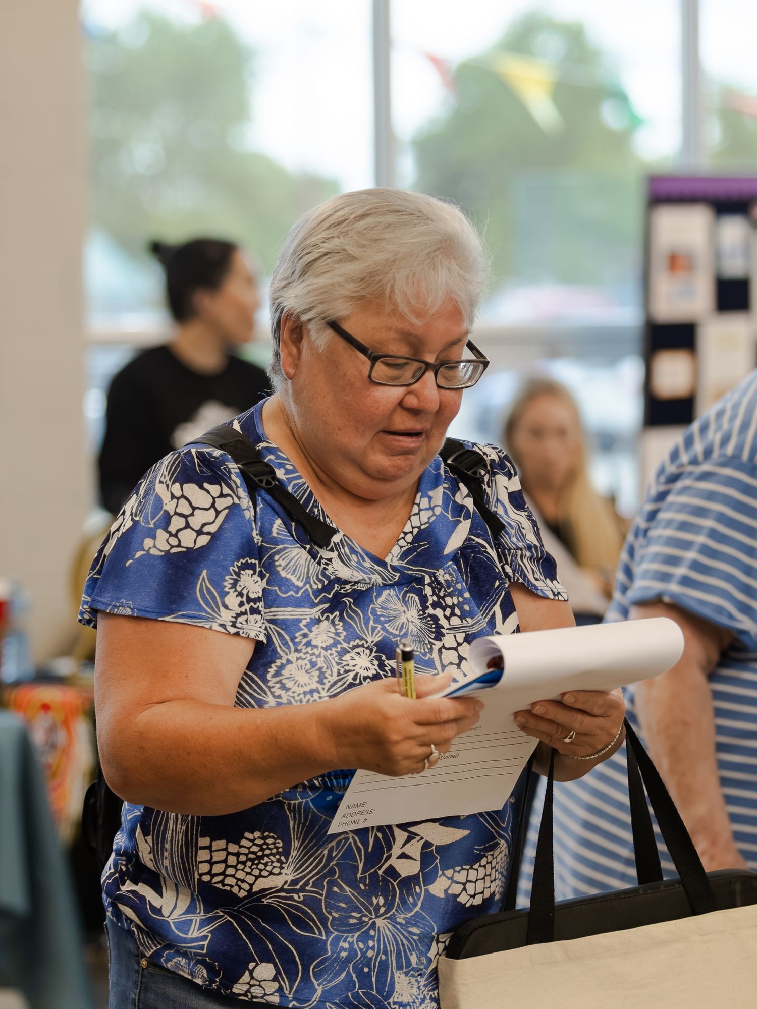 Senior woman in blue floral shirt reviewing documents at an indoor community health event.