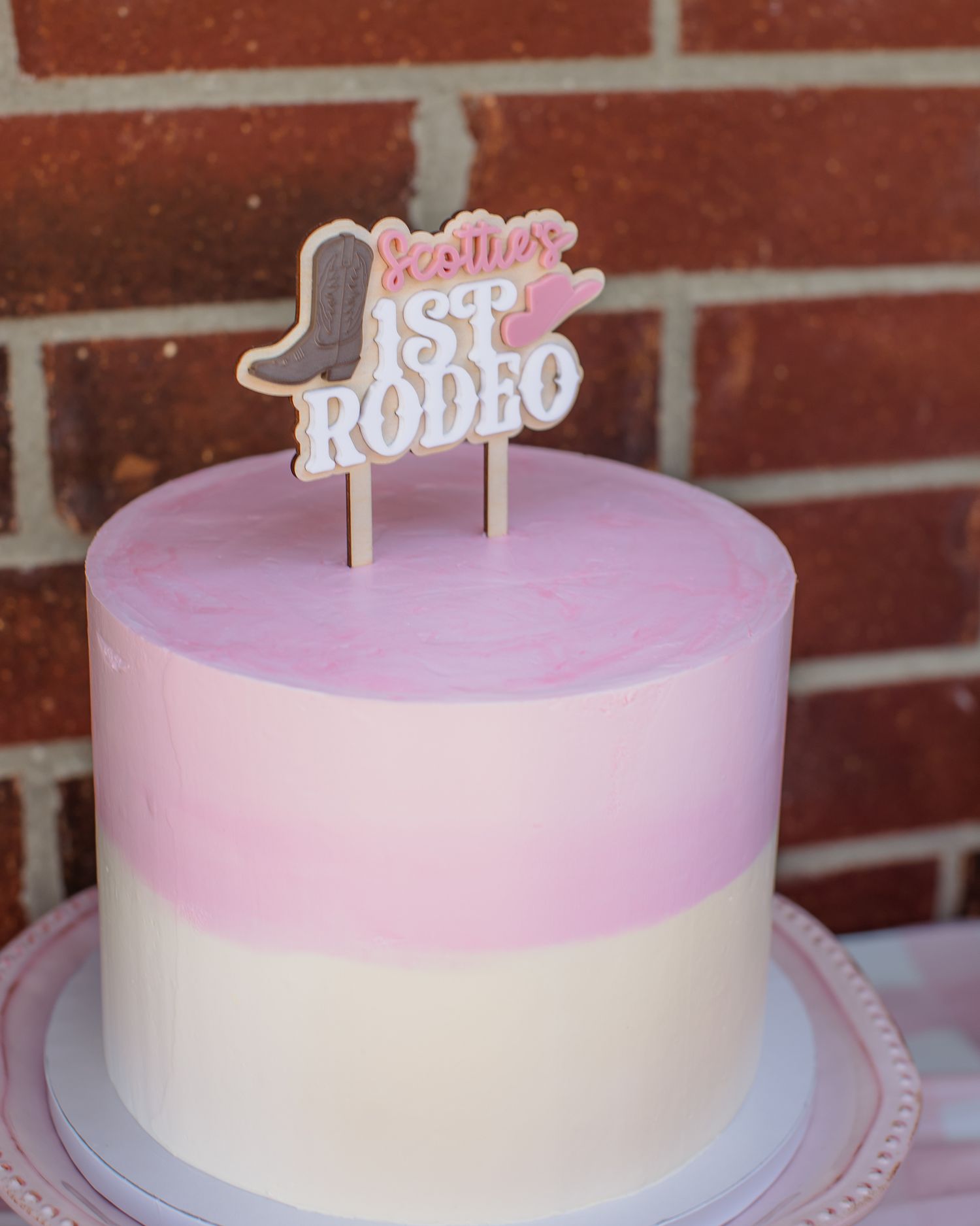 A pink and white cake with Scottie's 1st Rodeo cookie topper for a cowgirl themed first birthday party.