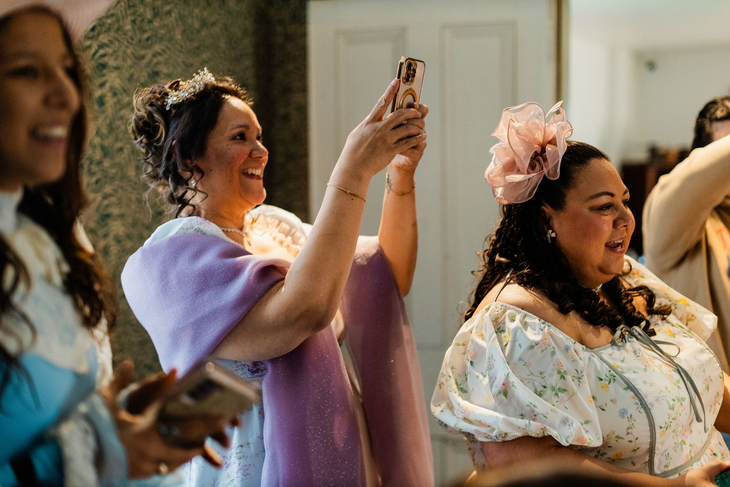 Women in colorful Regency-era gowns smile and take photos at an elegant event.