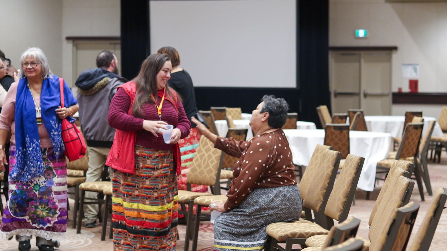 Conference hall setup with chairs and traditional indigenous decorations visible.
