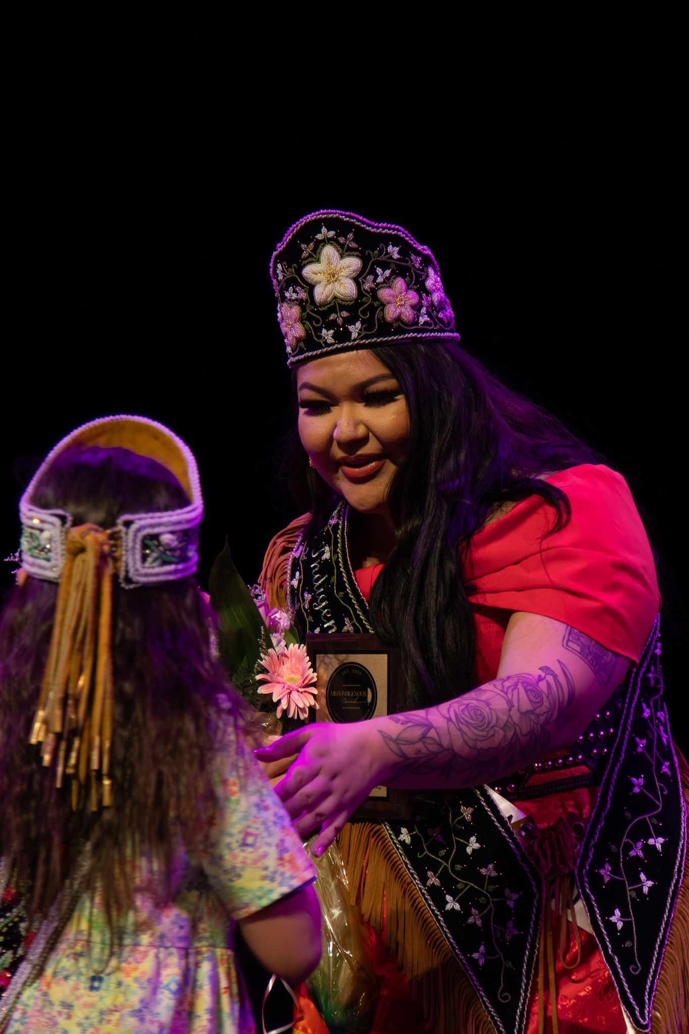A performer in regalia and crown during a cultural celebration on stage.