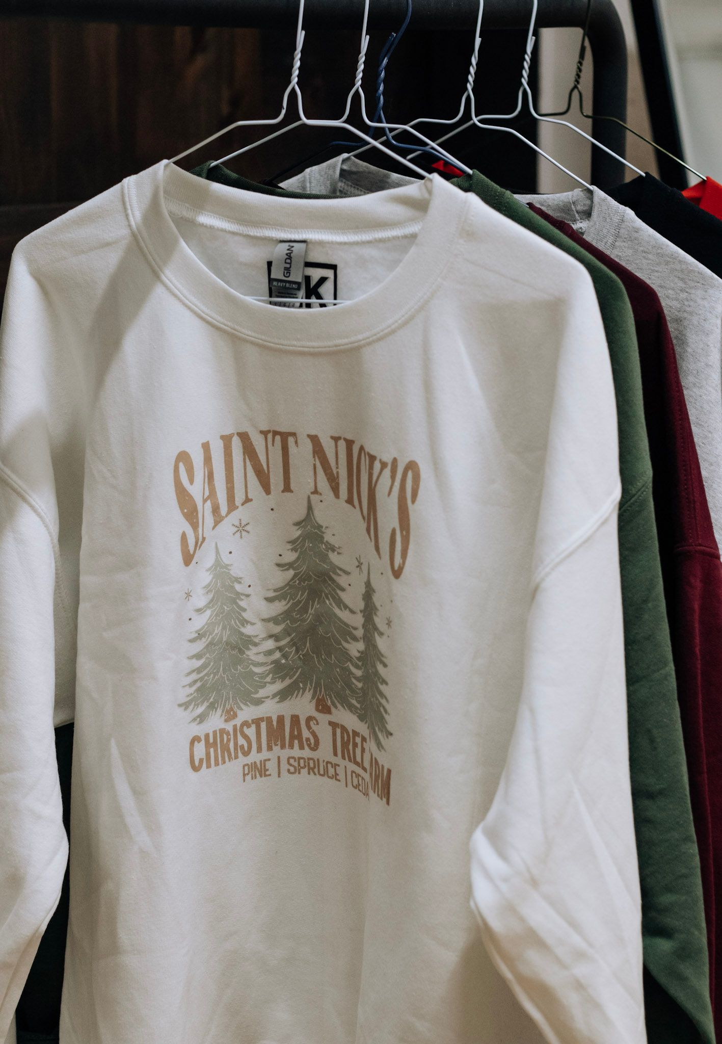 White Christmas-themed sweatshirts with pine tree designs hanging on retail display rack.