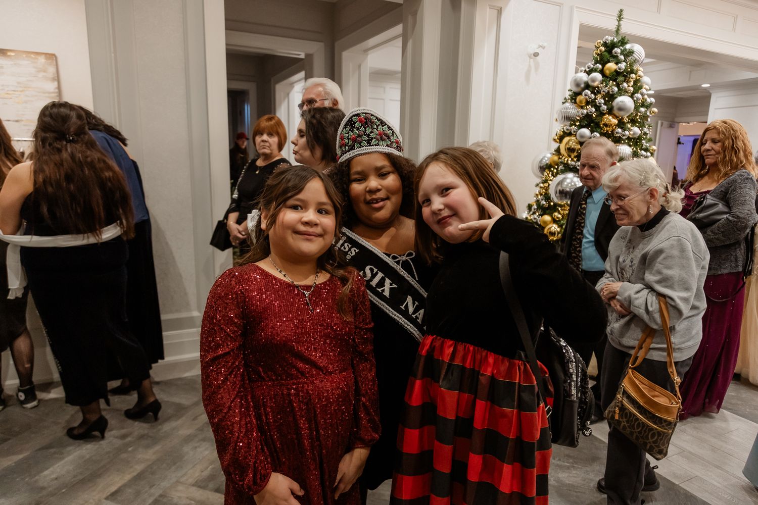 Three young friends celebrating at a holiday party with a Christmas tree in the background.