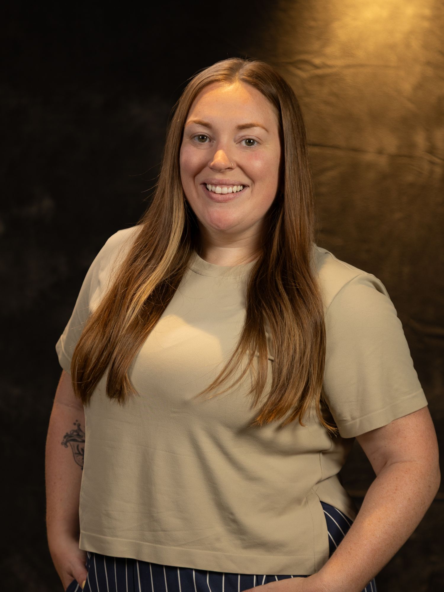 Professional studio portrait against dark background with dramatic lighting showing person in beige t-shirt.