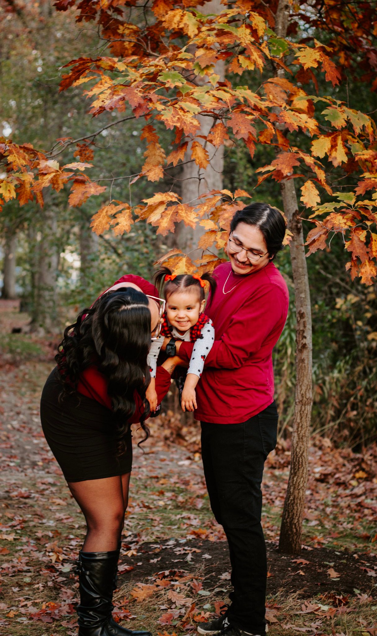 Playful family moment captured under vibrant autumn leaves on forest path.