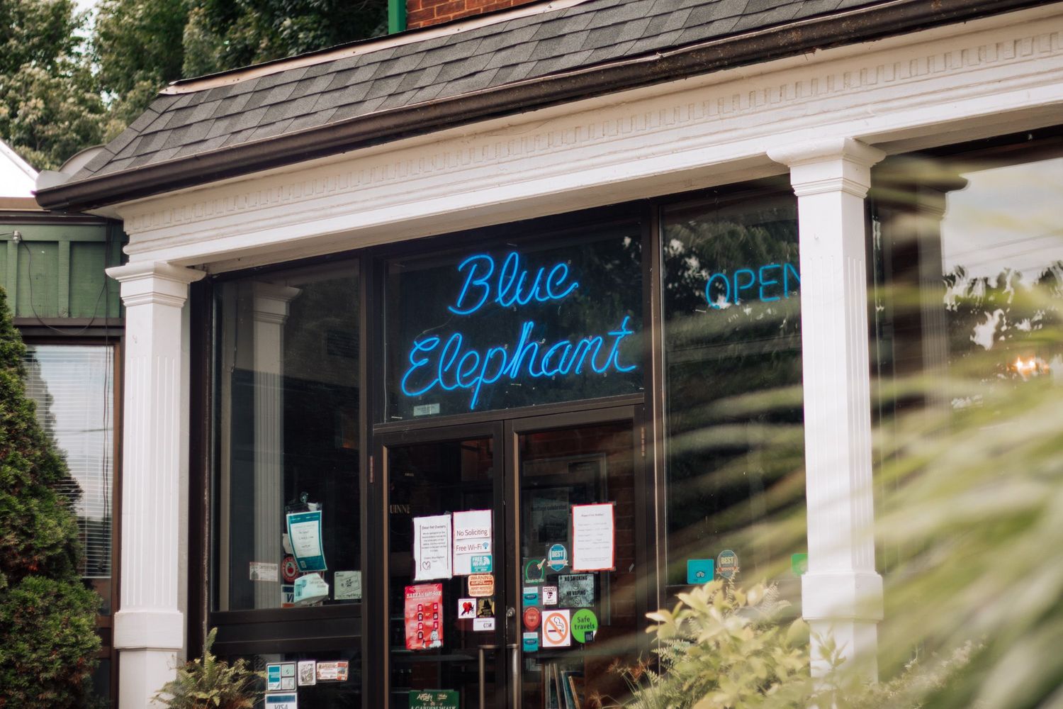 Blue Elephant restaurant storefront with neon blue sign displayed in large window of classic white-trimmed building.