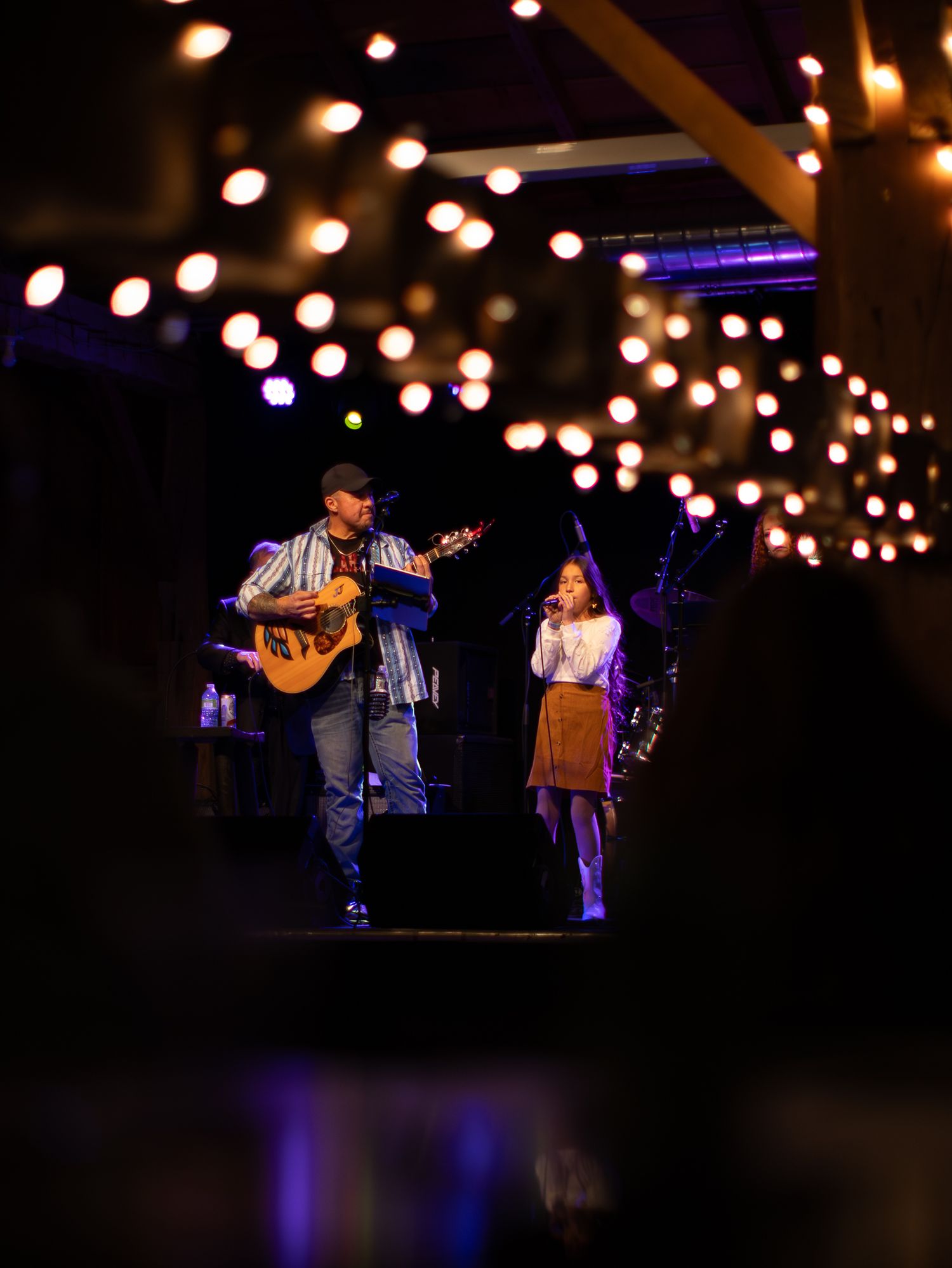 String lights hang above a dark performance space where musicians play on stage in the distance.